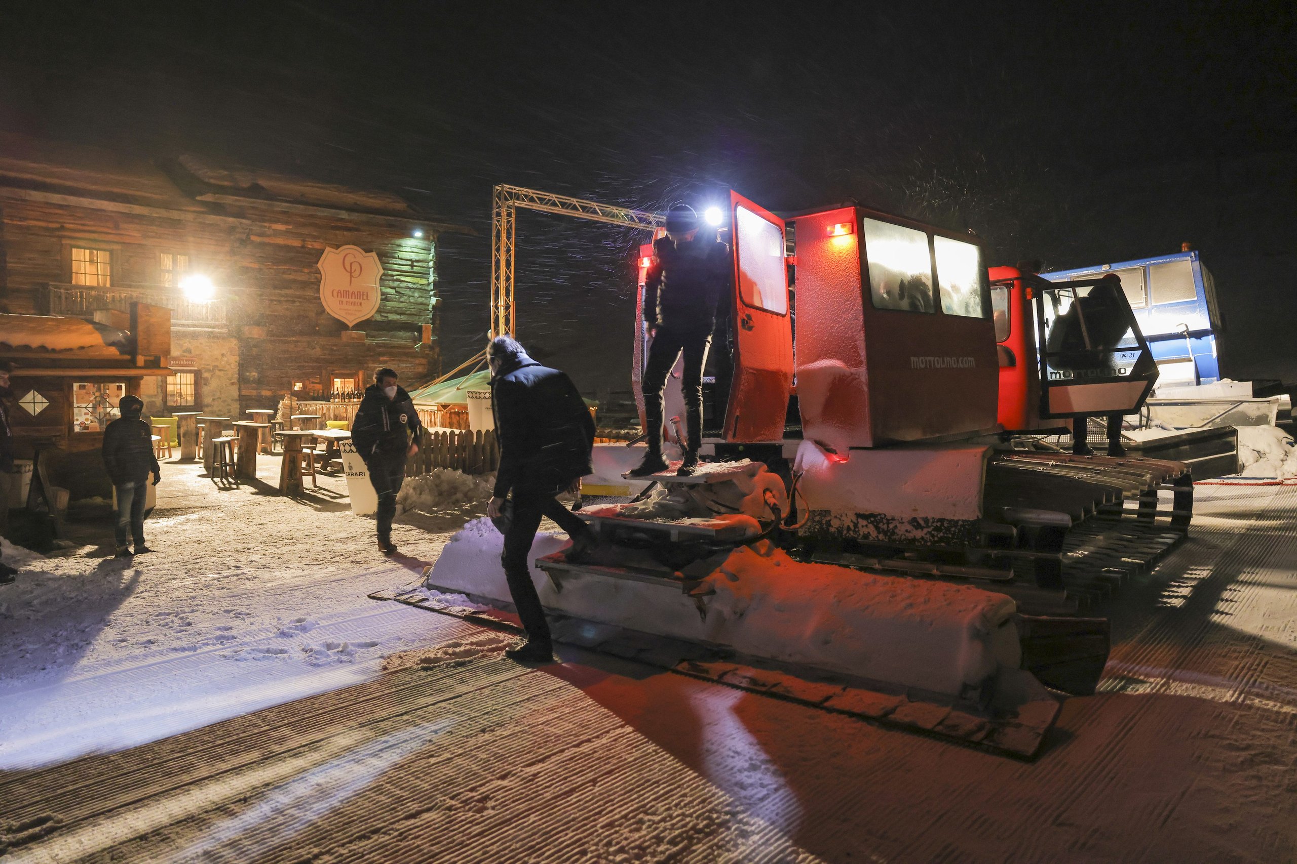 Accademia Neve 2022: What Lamborghini'S Ice Driving Program Actually Teaches Owners About Their Cars 13 Snow groomer illuminated by bright lights on a snowy path at night with rustic wooden building and falling snow at lamborghini accademia neve 2022