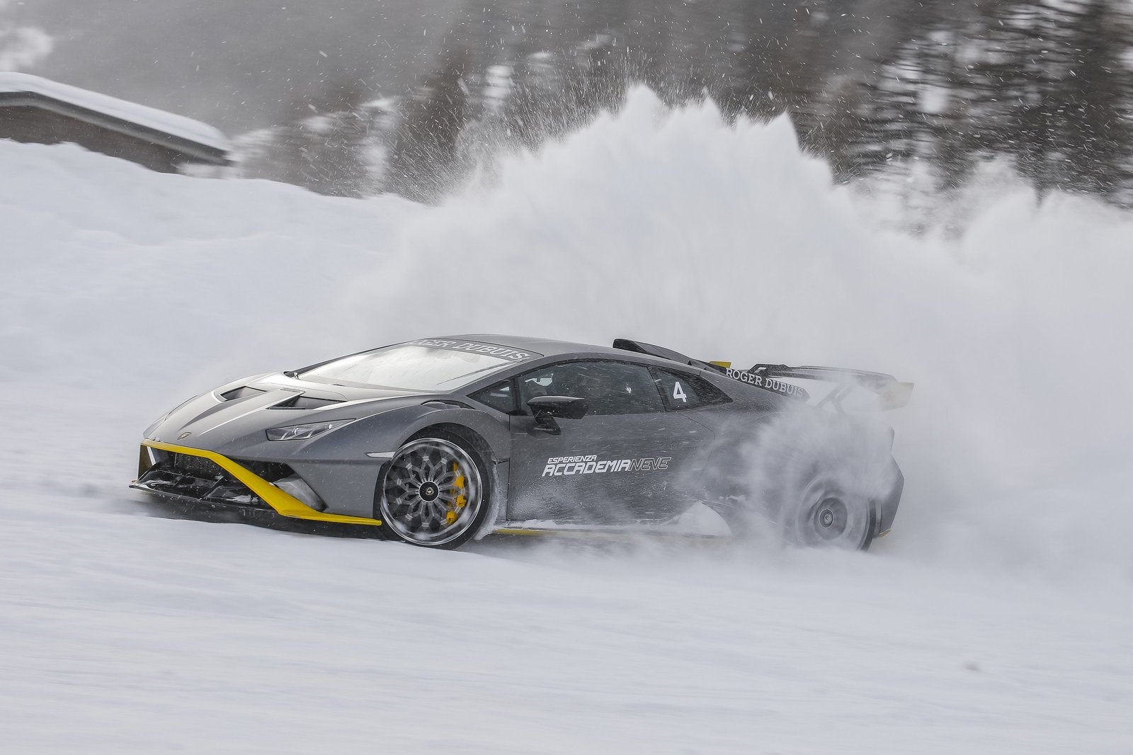 Grey Lamborghini Huracán STO with yellow accents drifting on a snowy track at Accademia Neve 2022, kicking up a large plume of snow