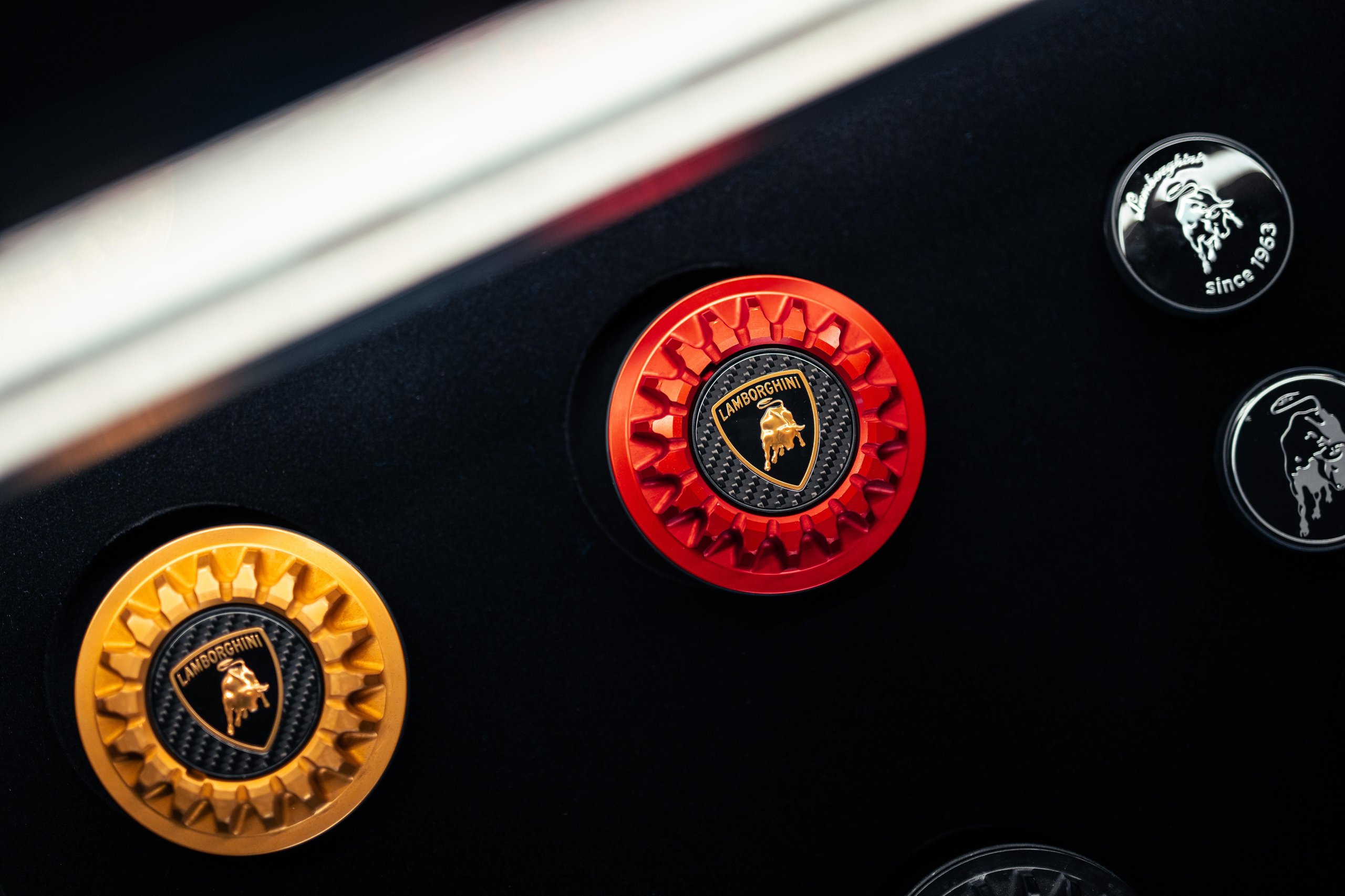 Close-up of lamborghini shield emblem samples including a red and black variant with carbon fiber texture