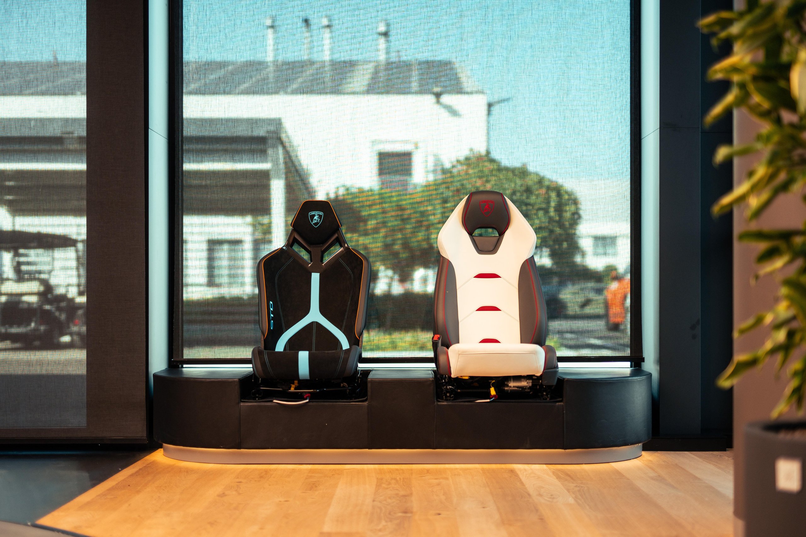 Two lamborghini racing seats on display, one black with blue accents and one white with red accents, showing contrasting stitching and alcantara options