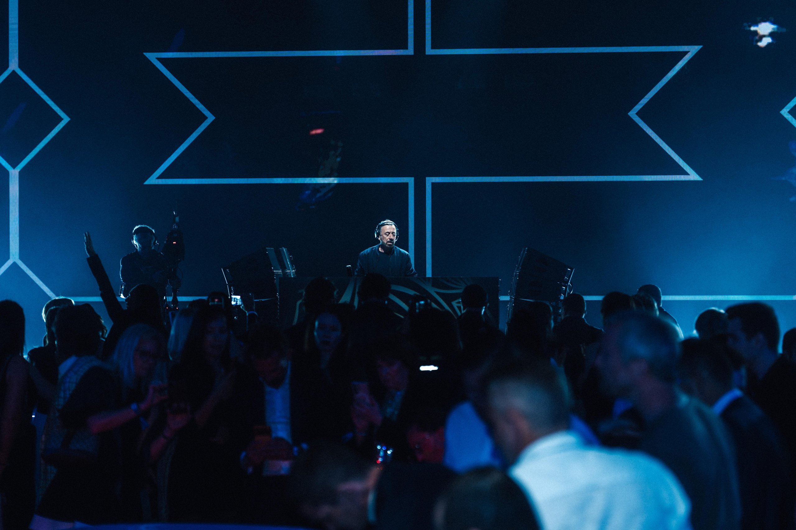 Why Lamborghini Hired Benny Benassi To Turn Arena Into A Homecoming For 6,000 Owners 7 Dj benny benassi performing on stage at lamborghini arena, seen from behind a crowd of attendees with blue geometric lighting
