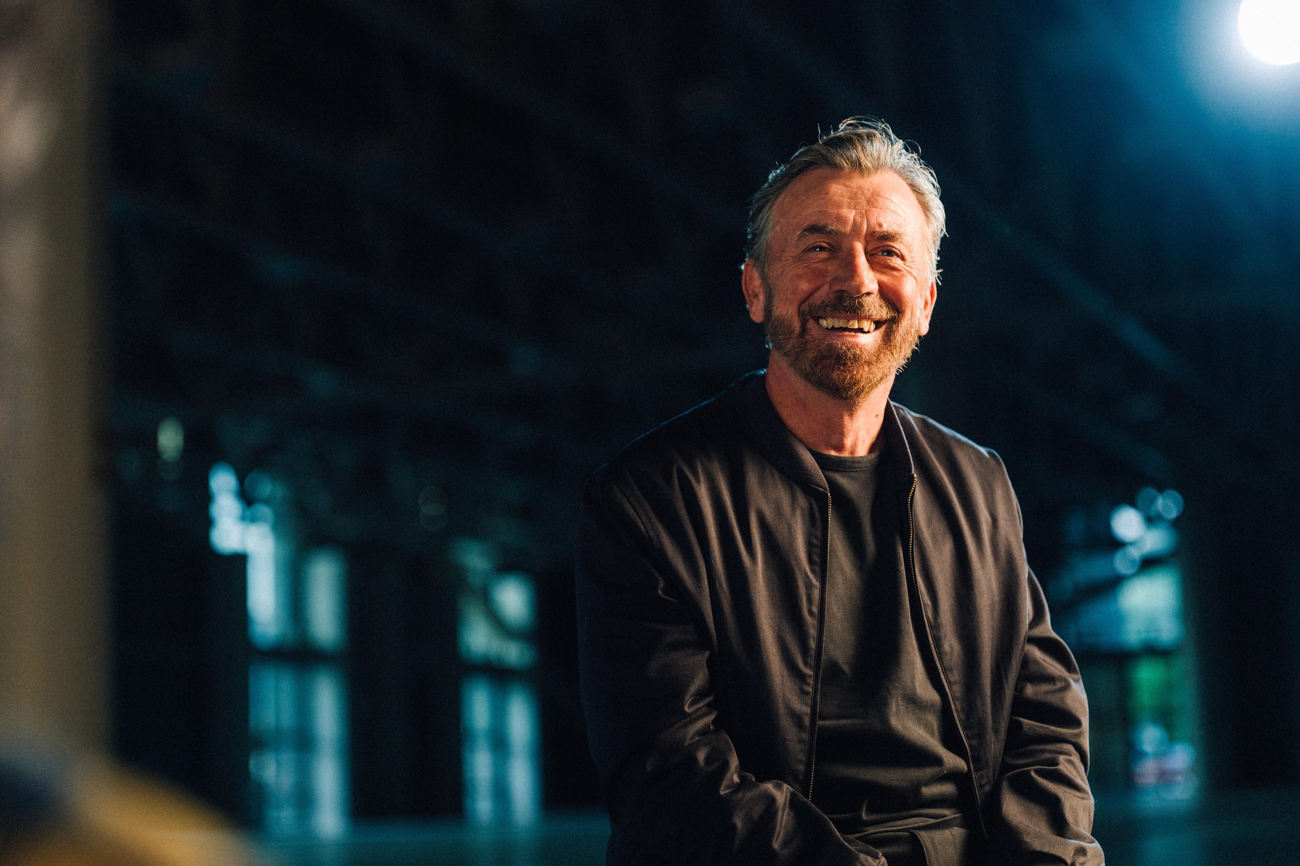 Why Lamborghini Hired Benny Benassi To Turn Arena Into A Homecoming For 6,000 Owners 5 Portrait of dj benny benassi smiling with a bright light source behind him in a dimly lit indoor setting