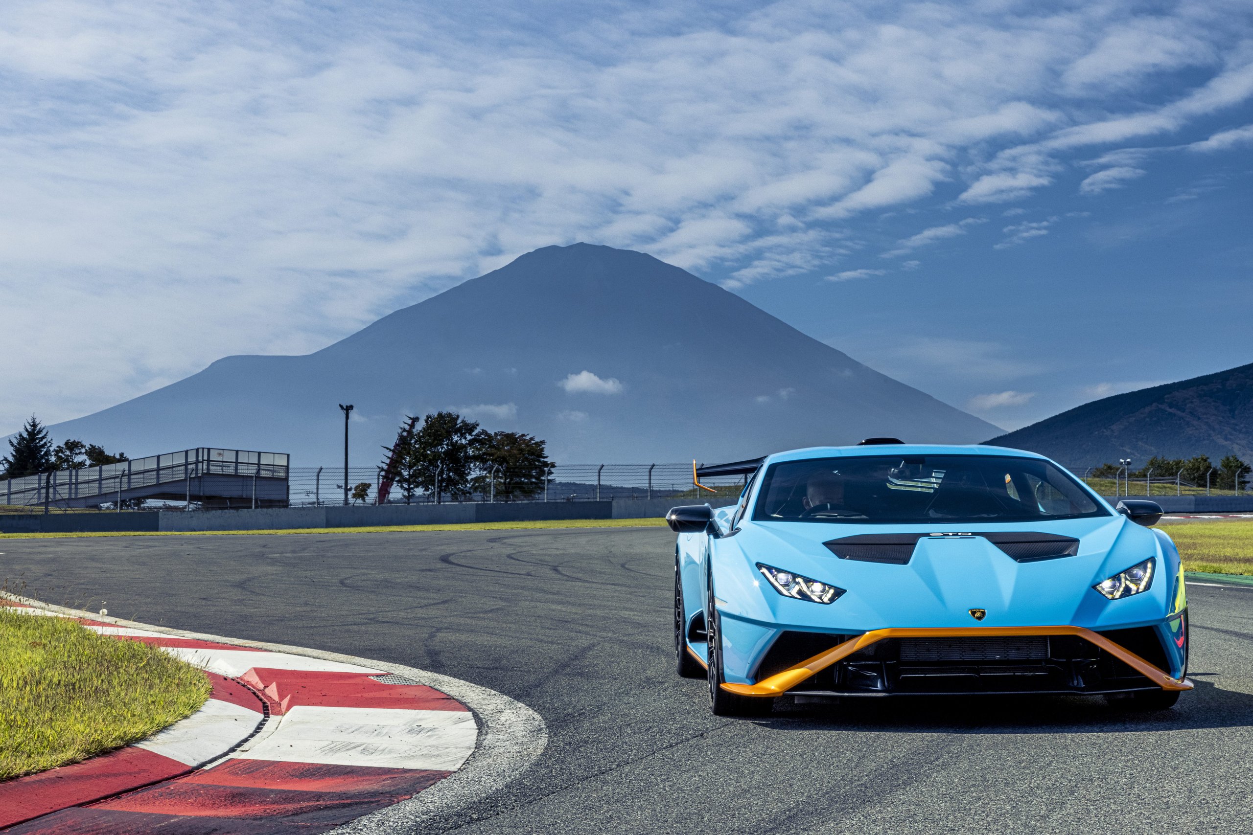 Lamborghini Doubled Its International Awards In 2021, And The Reasons Tell A Bigger Story Than The Trophies 5 Light blue lamborghini huracán sto with orange accents cornering on a racetrack with a mountain in the background