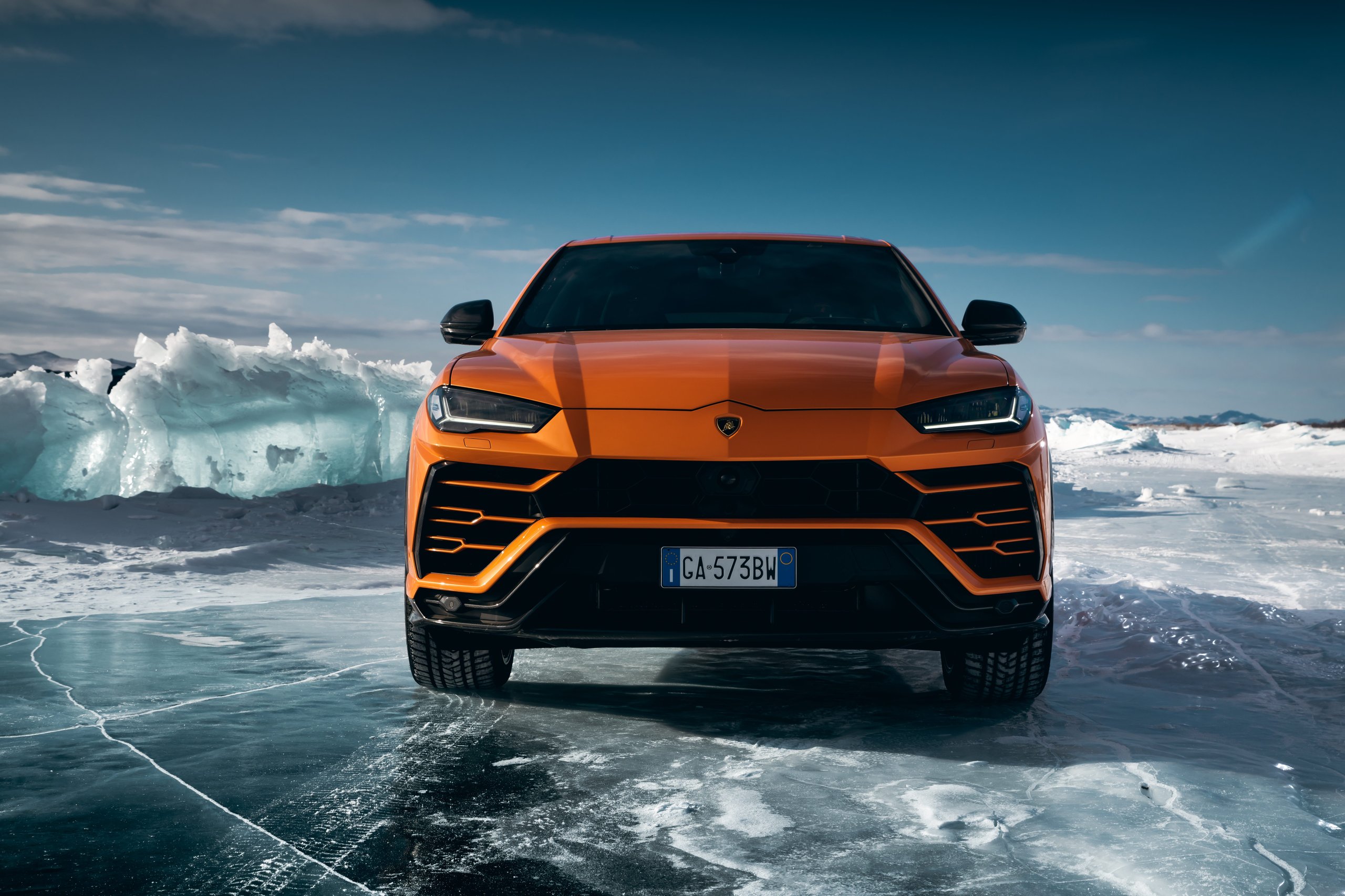 Lamborghini Doubled Its International Awards In 2021, And The Reasons Tell A Bigger Story Than The Trophies 3 Orange lamborghini urus parked on a frozen lake surrounded by large chunks of ice under a clear blue sky