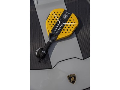Yellow and black babolat x lamborghini bl001 padel racquet resting on the hood of a grey lamborghini huracán tecnica