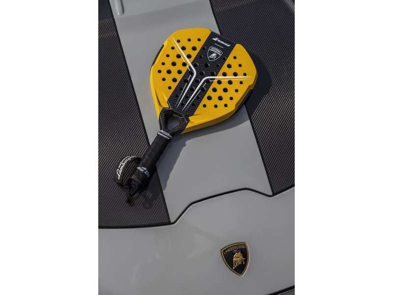 Yellow and black Babolat x Lamborghini BL001 padel racquet resting on the hood of a grey Lamborghini Huracán Tecnica