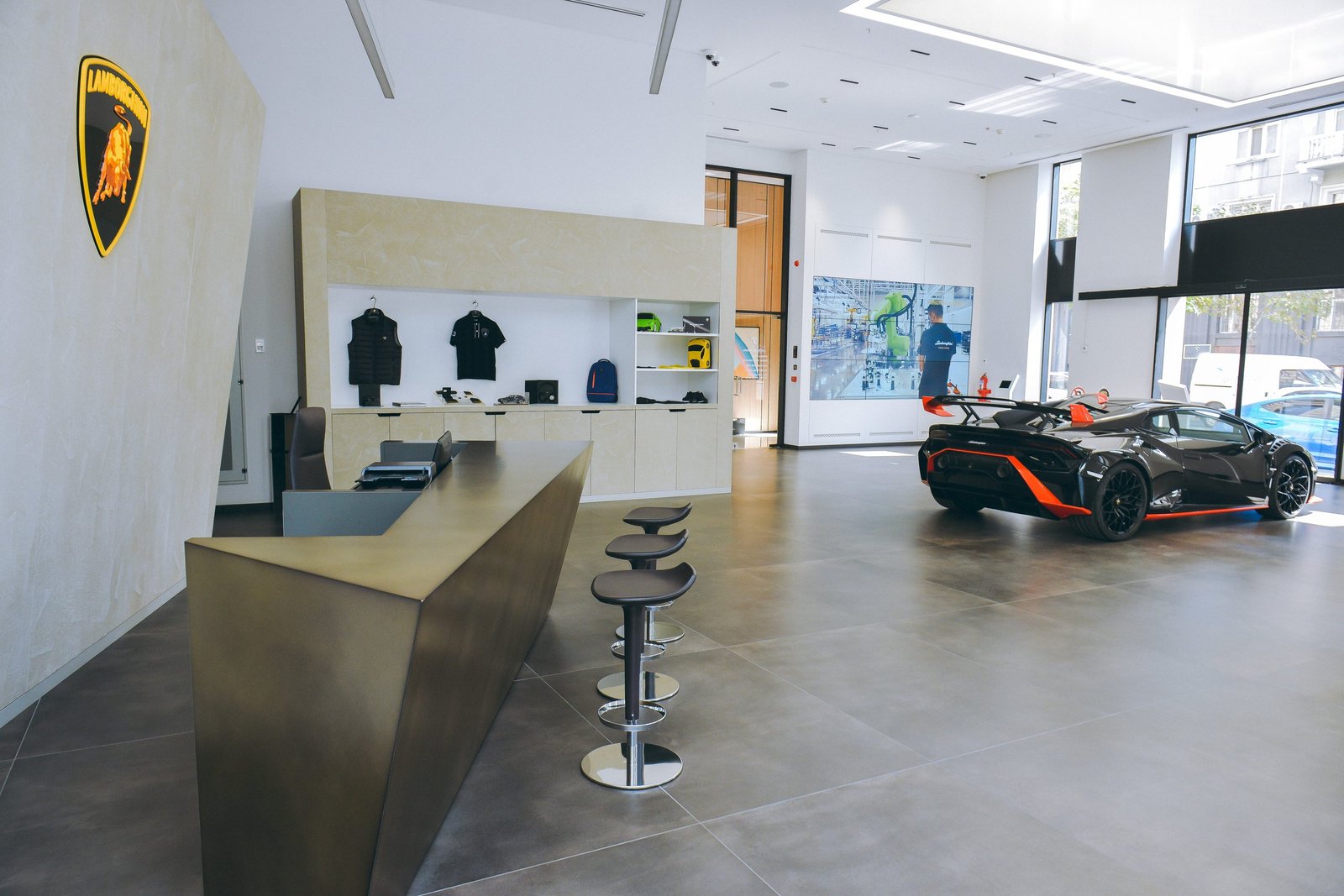 Interior of the new Lamborghini Baku showroom featuring a black and orange Huracán STO, reception desk, and merchandise display