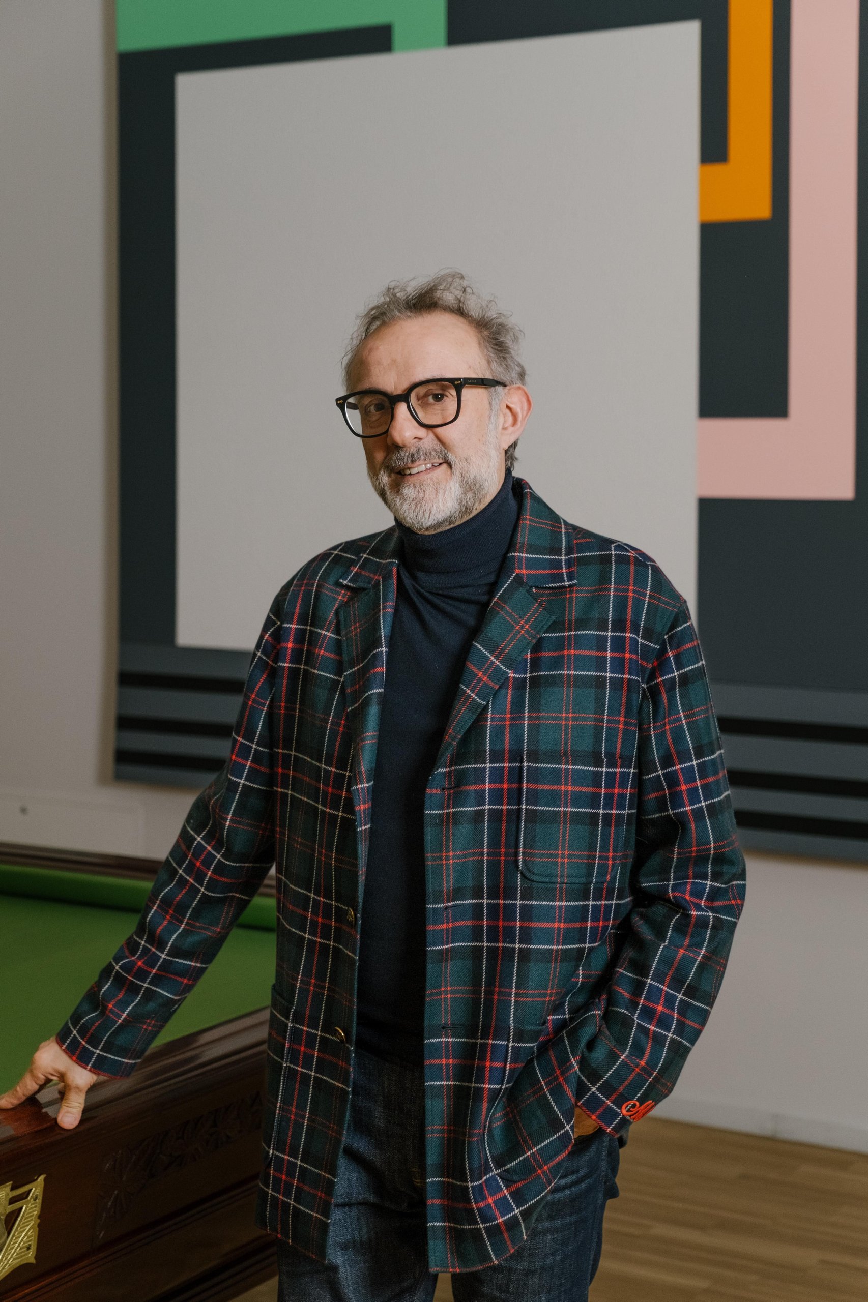 Why Lamborghini Put A Revuelto On A Serving Tray: The 'Beyond' Podcast'S Bottura Episode And The Brand Strategy Behind It 5 Massimo bottura smiling next to a billiard table with abstract art in the background, wearing a plaid jacket and dark turtleneck