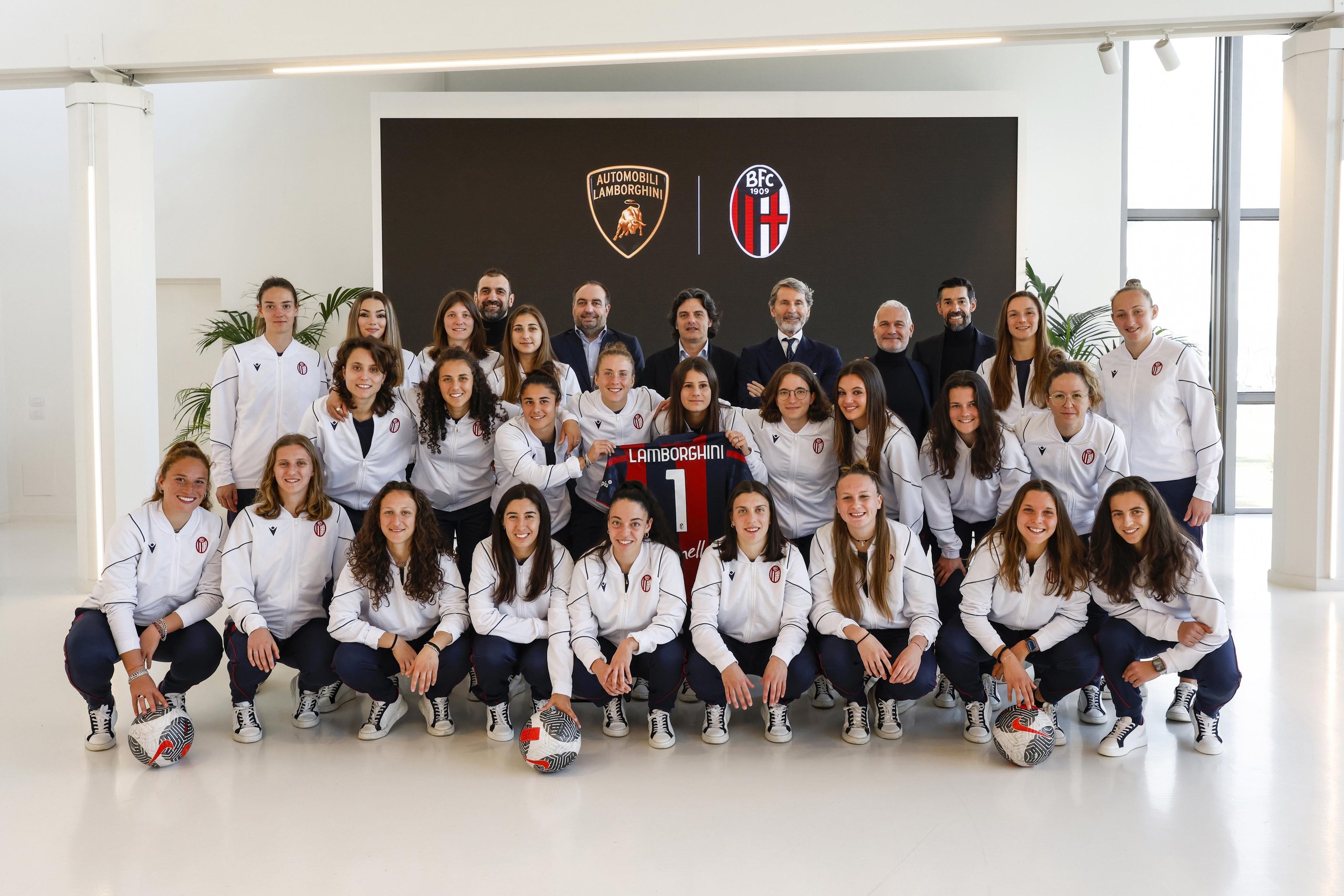 Lamborghini Brings Bologna'S Women'S Football Team To Sant'Agata, Signaling A Broader Brand Play 11 Group photo of bologna fc 1909 femminile players and lamborghini representatives indoors with partnership logos displayed on screen