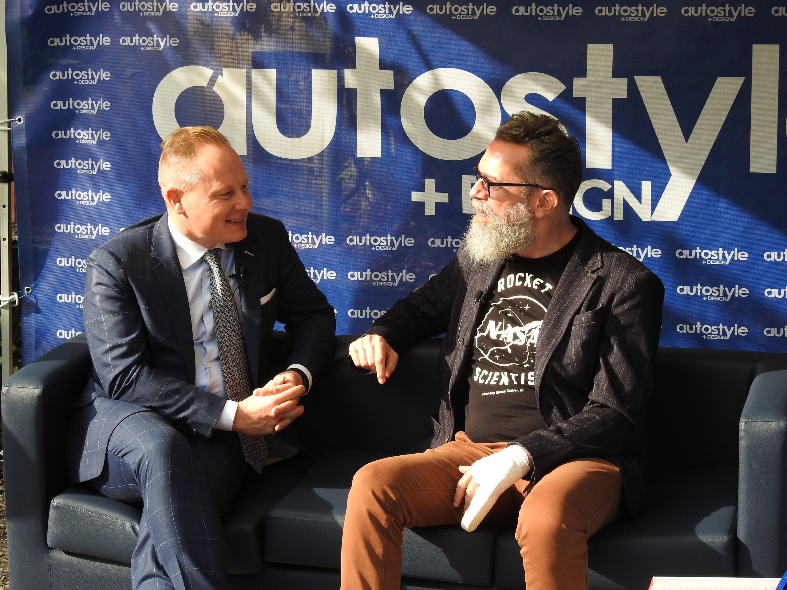 Mitja Borkert Used The Autostyle Stage To Explain Why Every Lamborghini Starts With A Single Line 3 Two men seated on a dark blue sofa in conversation at the autostyle design event with blue autostyle banner in background