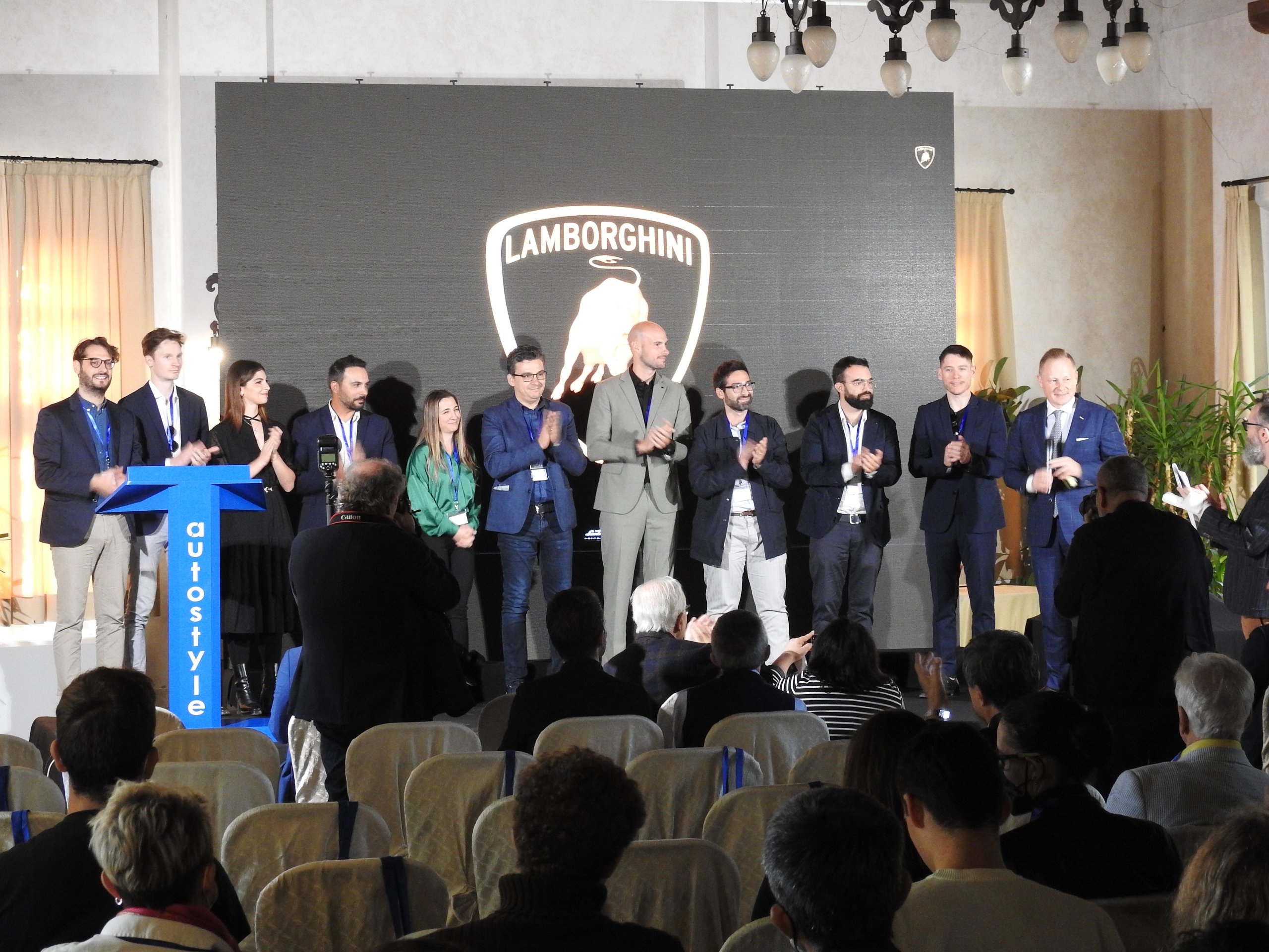Mitja Borkert Used The Autostyle Stage To Explain Why Every Lamborghini Starts With A Single Line 9 Group of people standing on stage in front of lamborghini logo screen receiving applause from audience at autostyle event