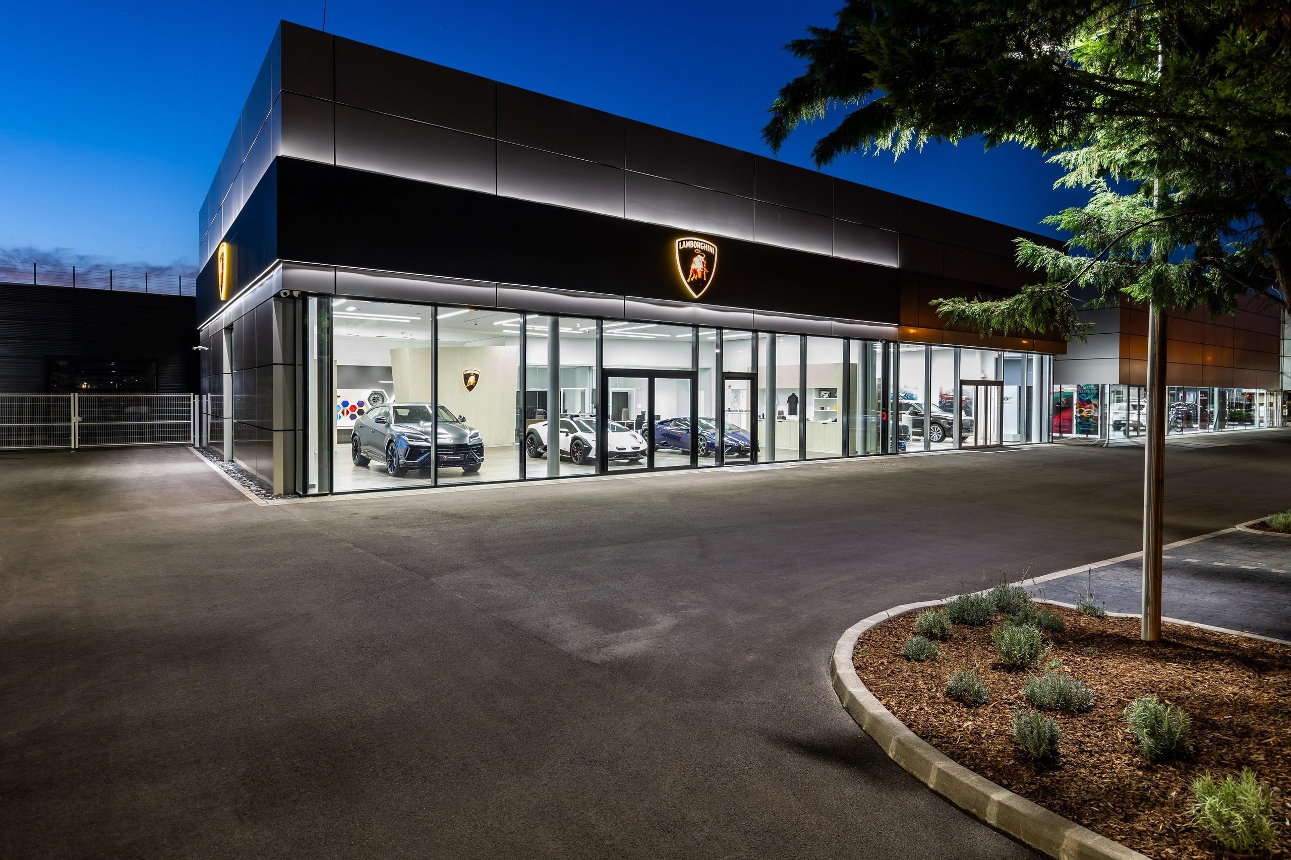 Budapest Gets Its First Lamborghini Showroom, And The Revuelto Came Along To Make The Point 3 Exterior night view of the illuminated lamborghini budapest showroom with vehicles visible through large glass windows