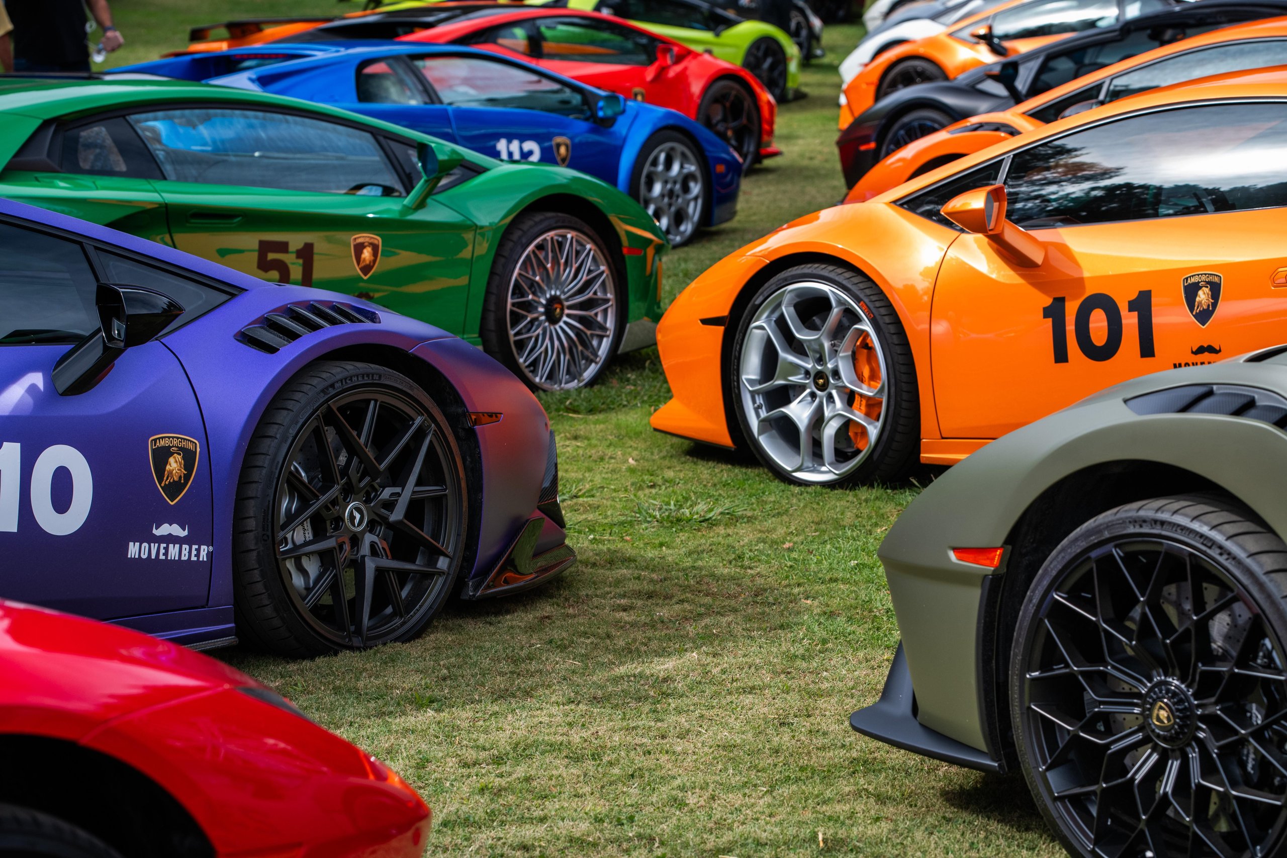 200 Mustache-Wearing Lamborghinis Took Over Malibu, And The Ceo Was Leading The Pack 9 Several colorful lamborghini huracán models in purple, green, blue, and orange parked on grass with movember branding