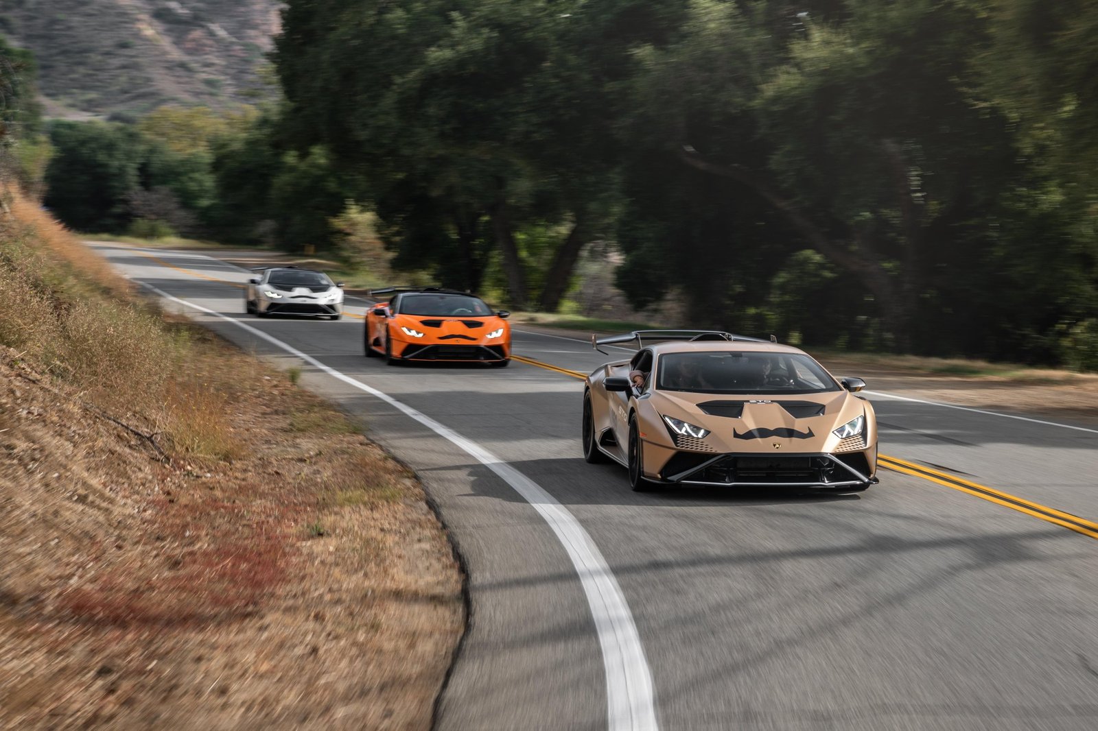 Three Lamborghini Huracán models driving in convoy through Malibu canyons with Movember mustache decals during the 2023 Bull Run