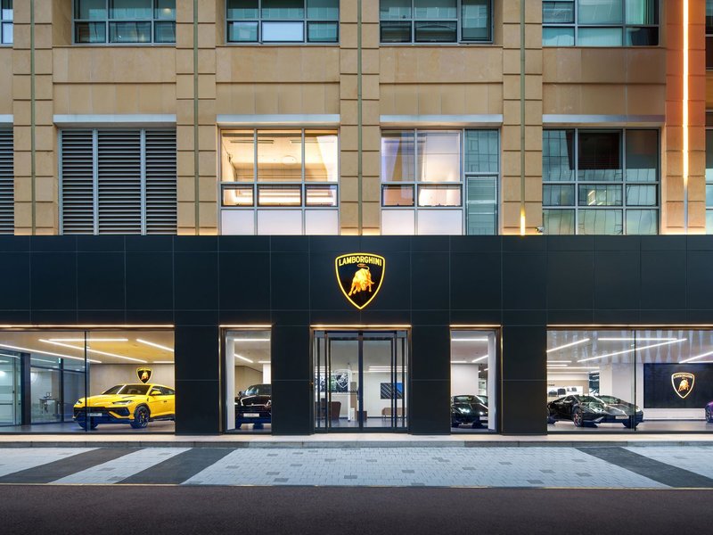 The new Lamborghini Bundang dealership at night, its illuminated logo and black facade framing luxury vehicles visible through floor-to-ceiling glass windows