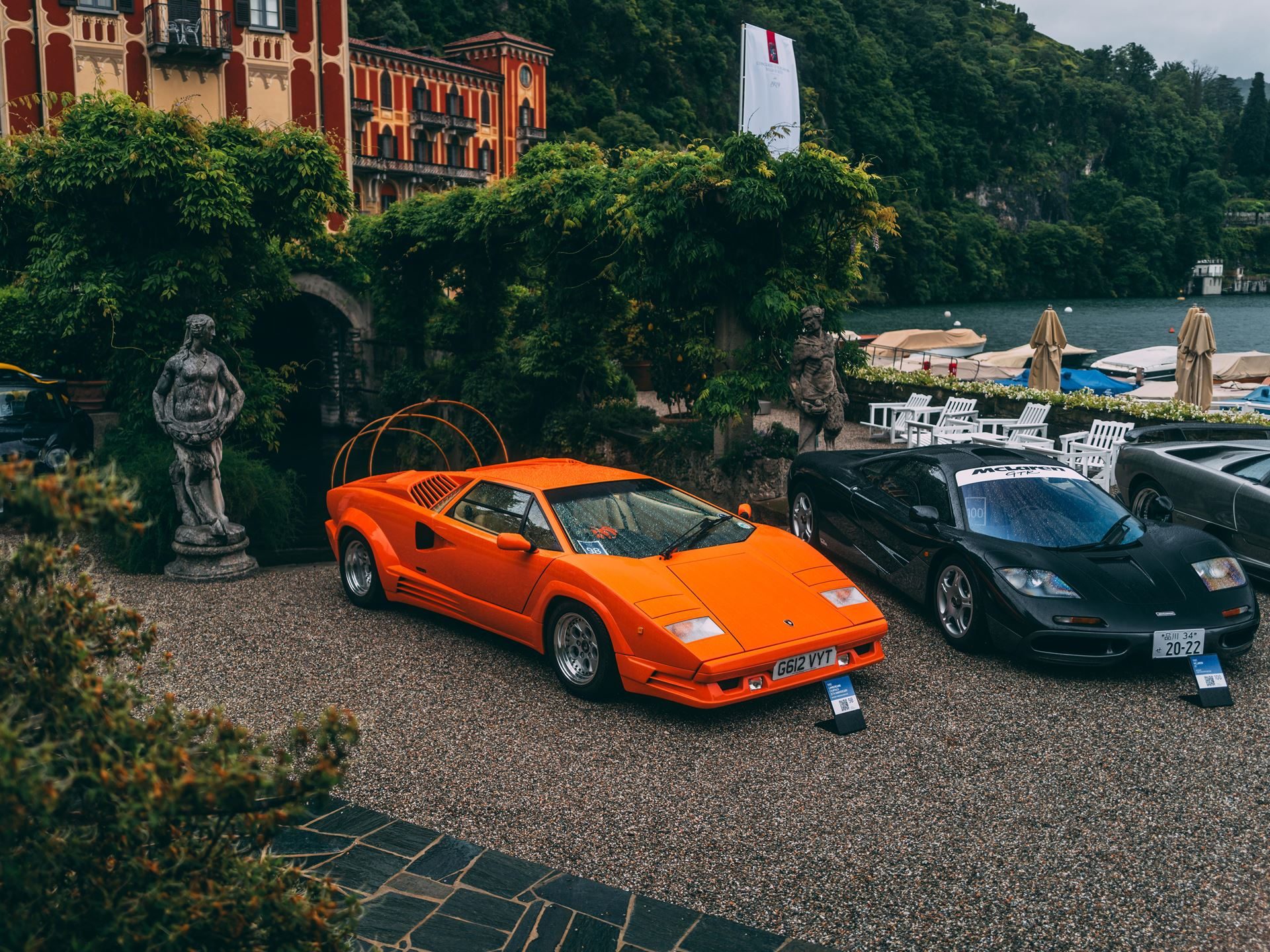 Two Trophies, Four V12S: Lamborghini'S Strongest Villa D'Este Showing In Years 5 Orange lamborghini countach 25th anniversary displayed on gravel at villa d'este with a historic building and lake in the background