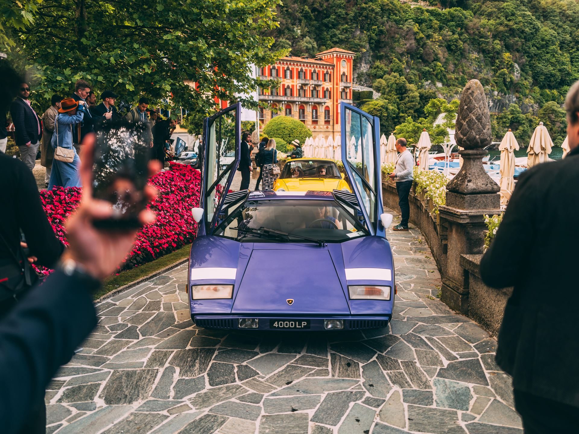 Purple lamborghini countach lp 400 with scissor doors open on a stone path surrounded by spectators at villa d'este