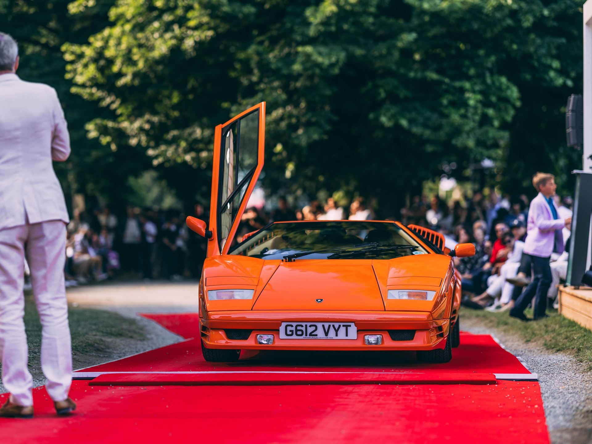 Orange lamborghini countach 25th anniversary with scissor door open at an outdoor concours event