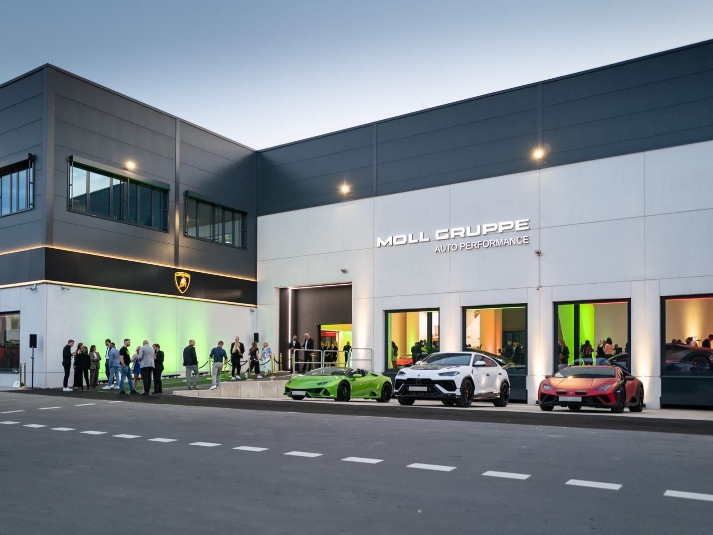 Exterior of the new lamborghini cologne dealership at dusk with guests and lamborghini vehicles parked outside during the grand opening event