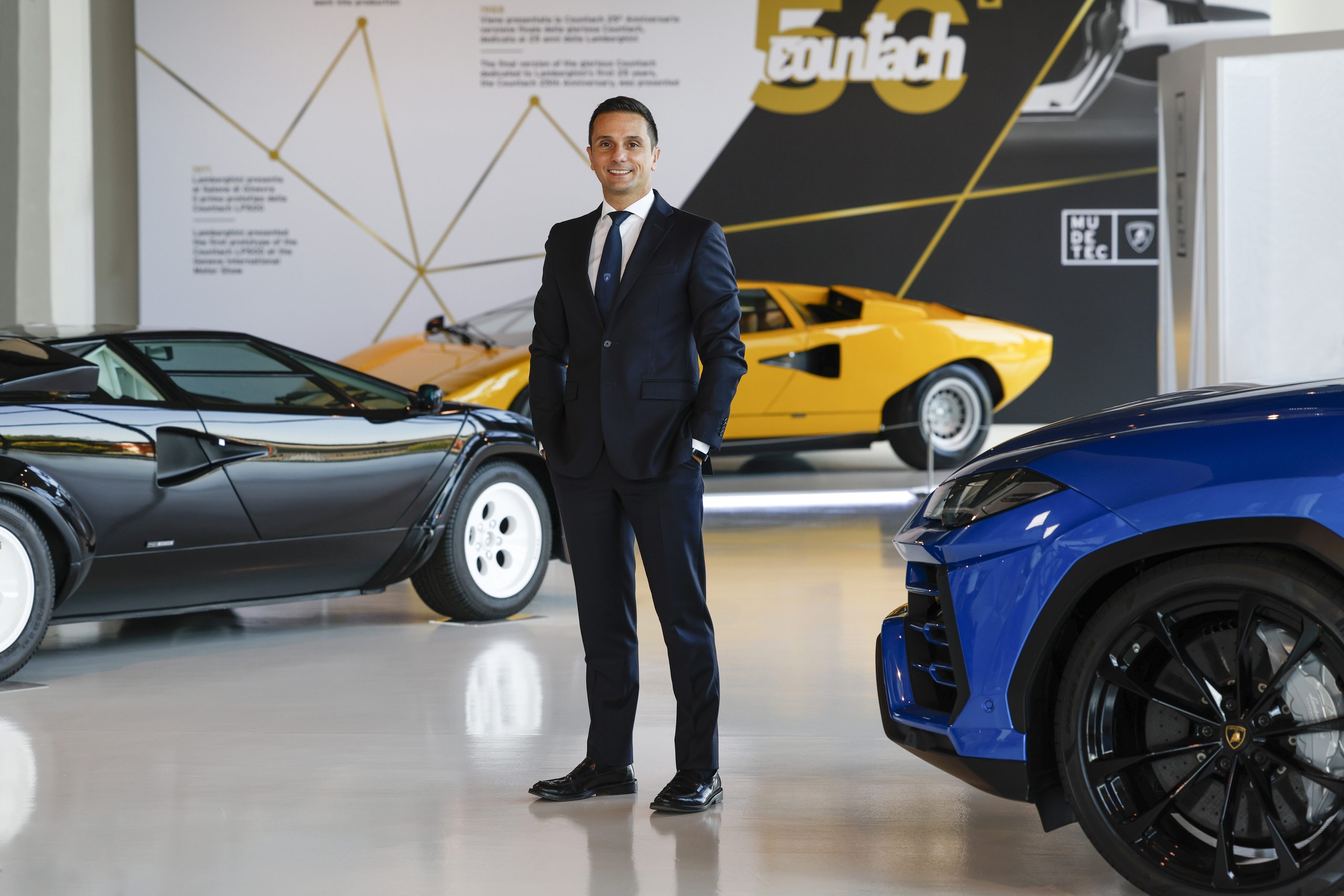Lamborghini'S New Procurement Chief Built Polo Storico. Now He Sources Parts For The Electric Era. 5 Paolo gabrielli standing between a black and yellow lamborghini countach with a blue urus in the foreground inside a museum setting