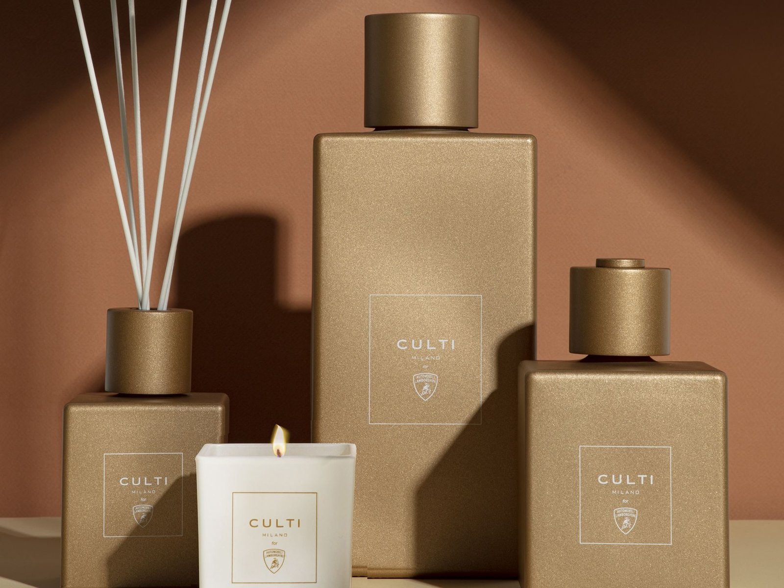 Culti Milano for Automobili Lamborghini home fragrance collection featuring a lit candle and three diffusers in matte gold finish
