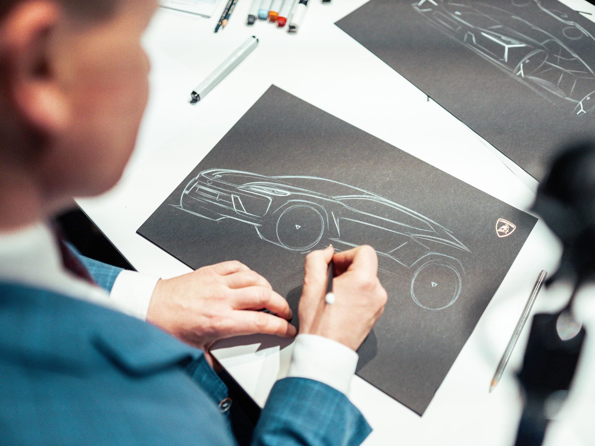 Lamborghini Day Uk Turned A Hybrid Reveal Into A Full Brand Experience, And That Was The Point 11 Designer sketching the side profile of a lamborghini urus se on black paper at a centro stile workshop during lamborghini day uk 2024