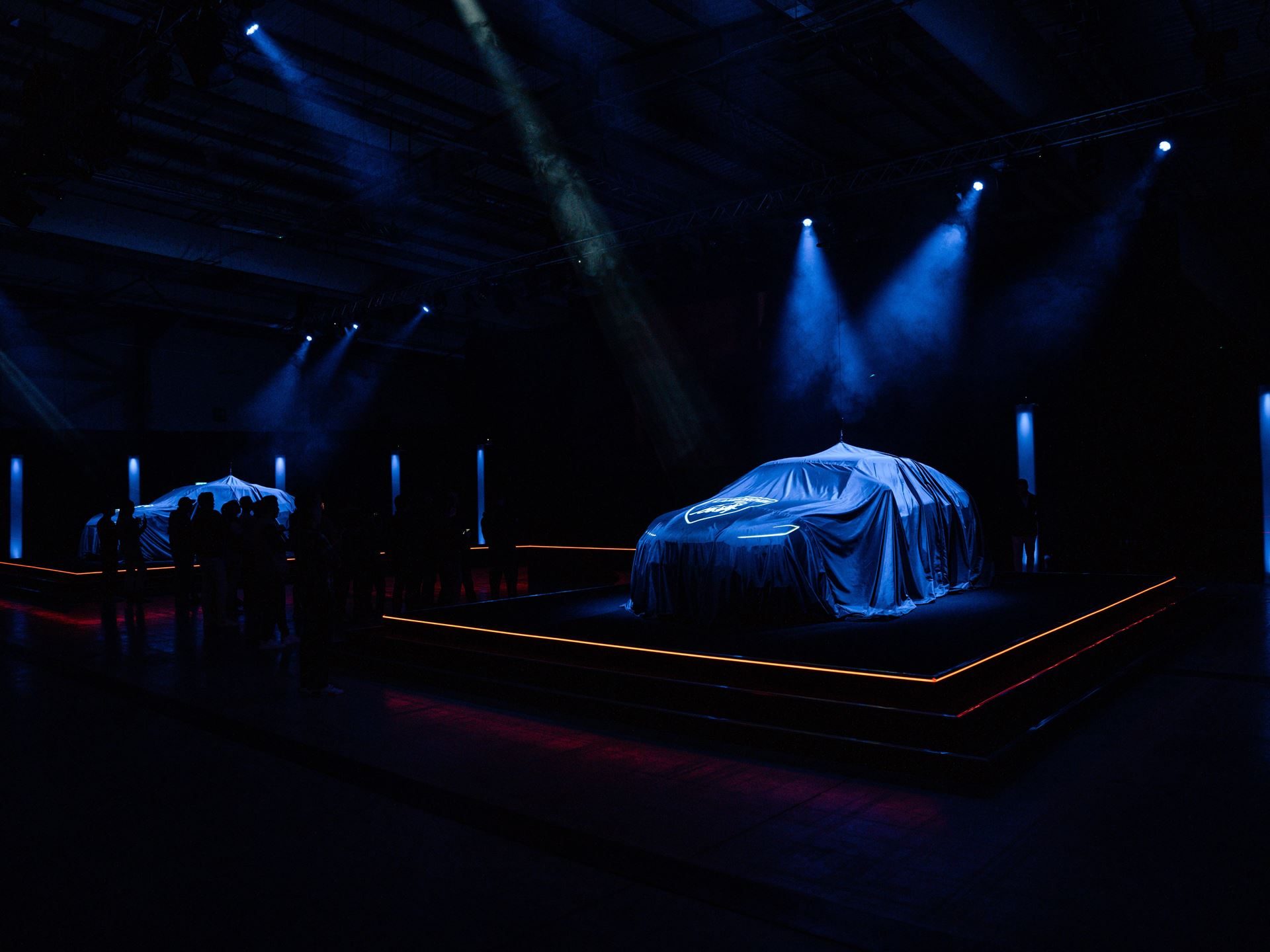 Lamborghini Day Uk Turned A Hybrid Reveal Into A Full Brand Experience, And That Was The Point 3 Two covered lamborghini urus se vehicles on elevated platforms at lamborghini day uk 2024, with a crowd gathered for the reveal