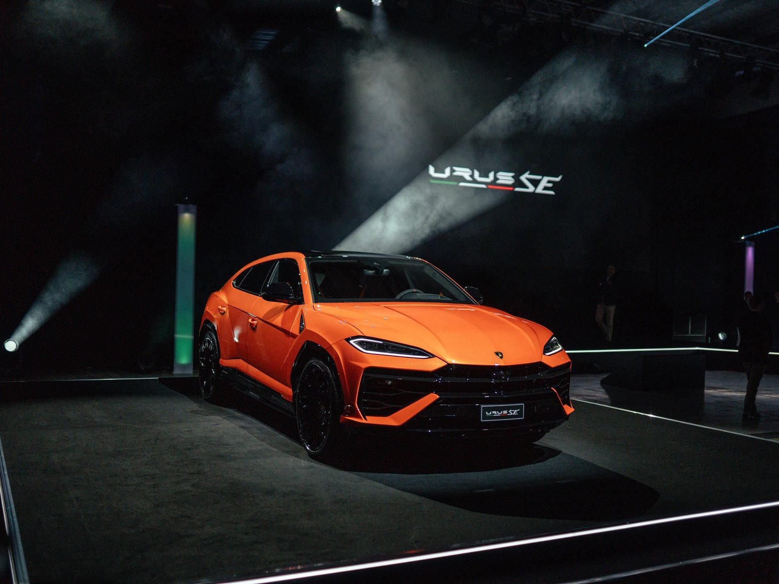 Orange Lamborghini Urus SE under spotlights on stage at Lamborghini Day UK 2024 with URUS SE projected in the background