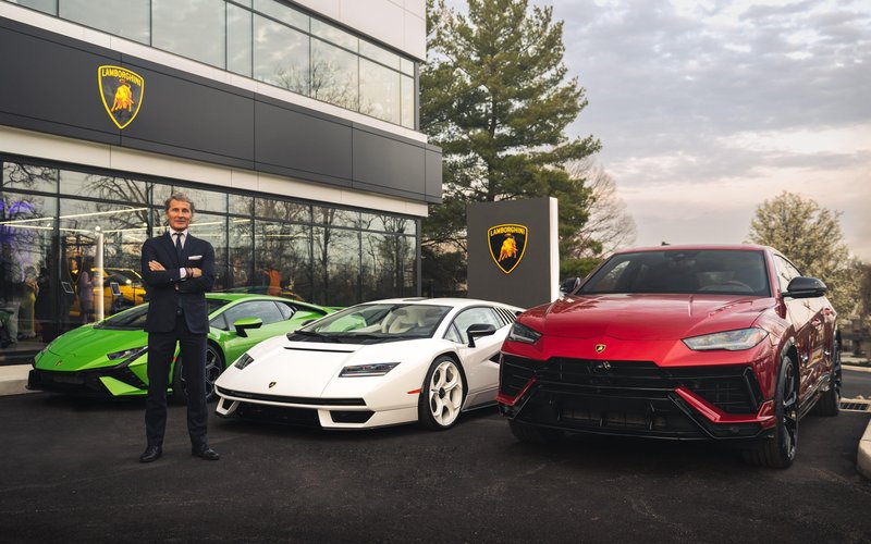 A Lamborghini executive stands before a green Huracán, white Countach LPI 800-4, and red Urus at a new dealership opening event