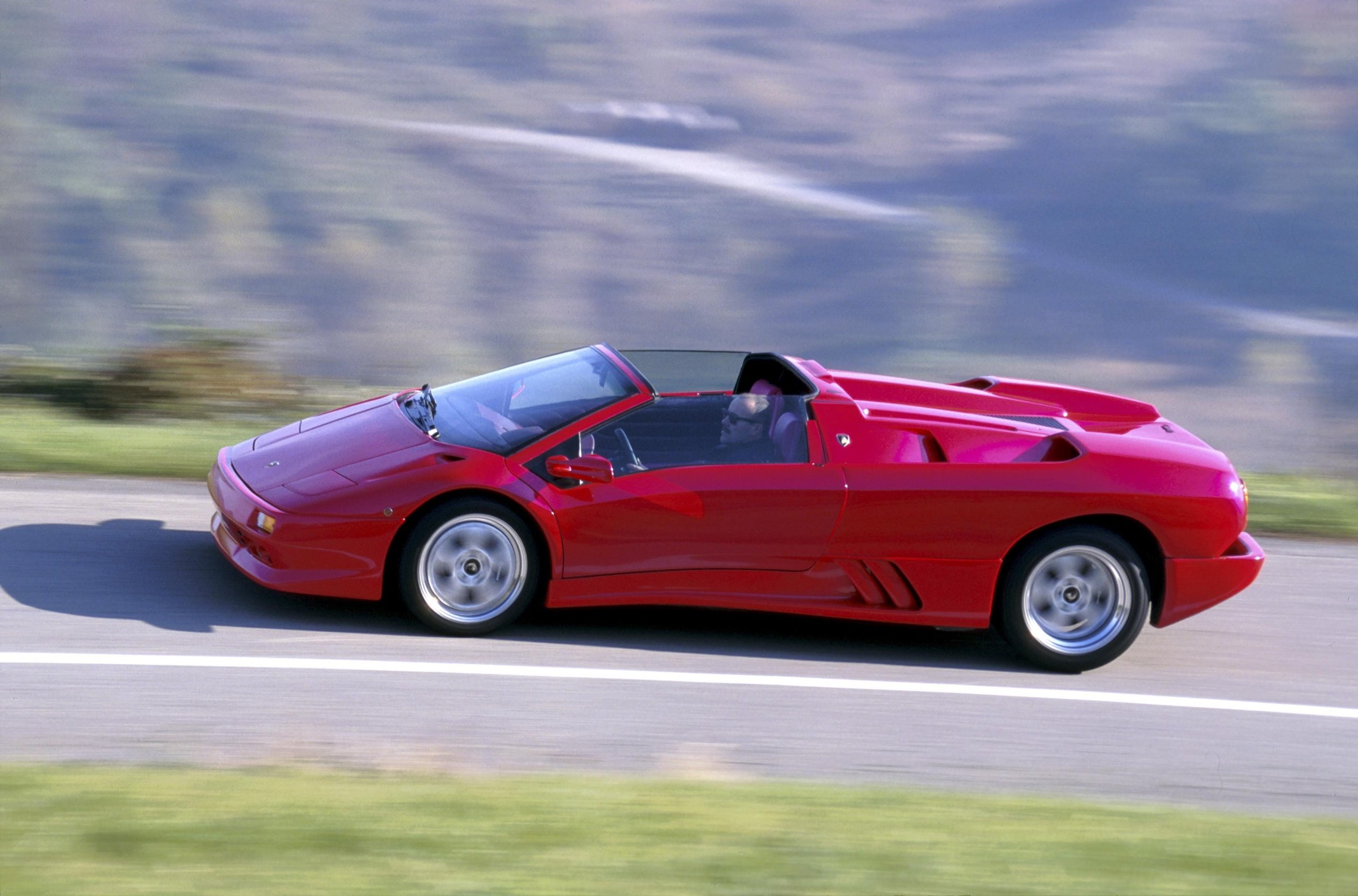Red Lamborghini Diablo Roadster in motion on a winding road with blurred background indicating speed
