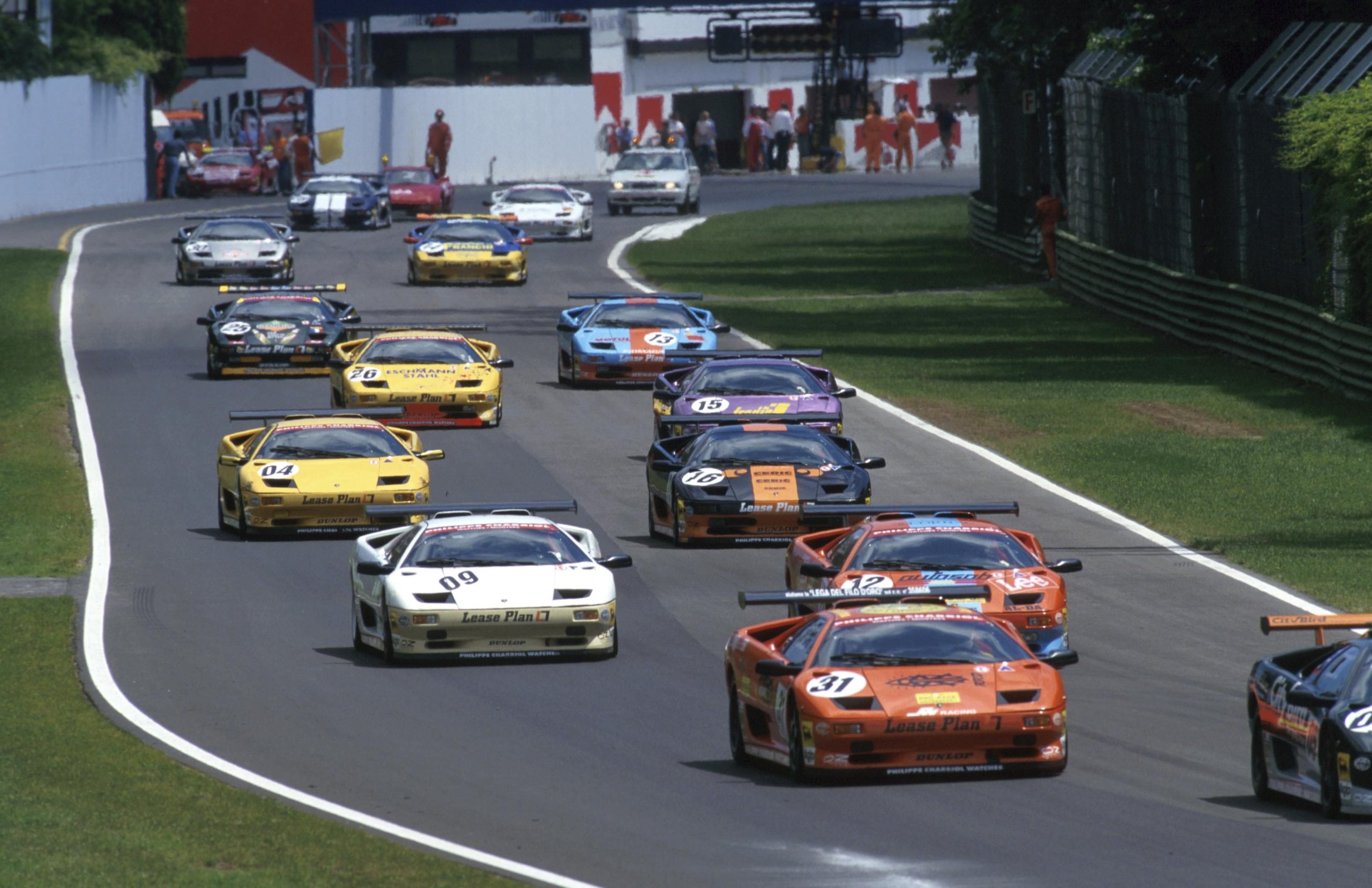 Multiple Lamborghini Diablo GTR race cars in various colors on a race track during competition with spectators visible