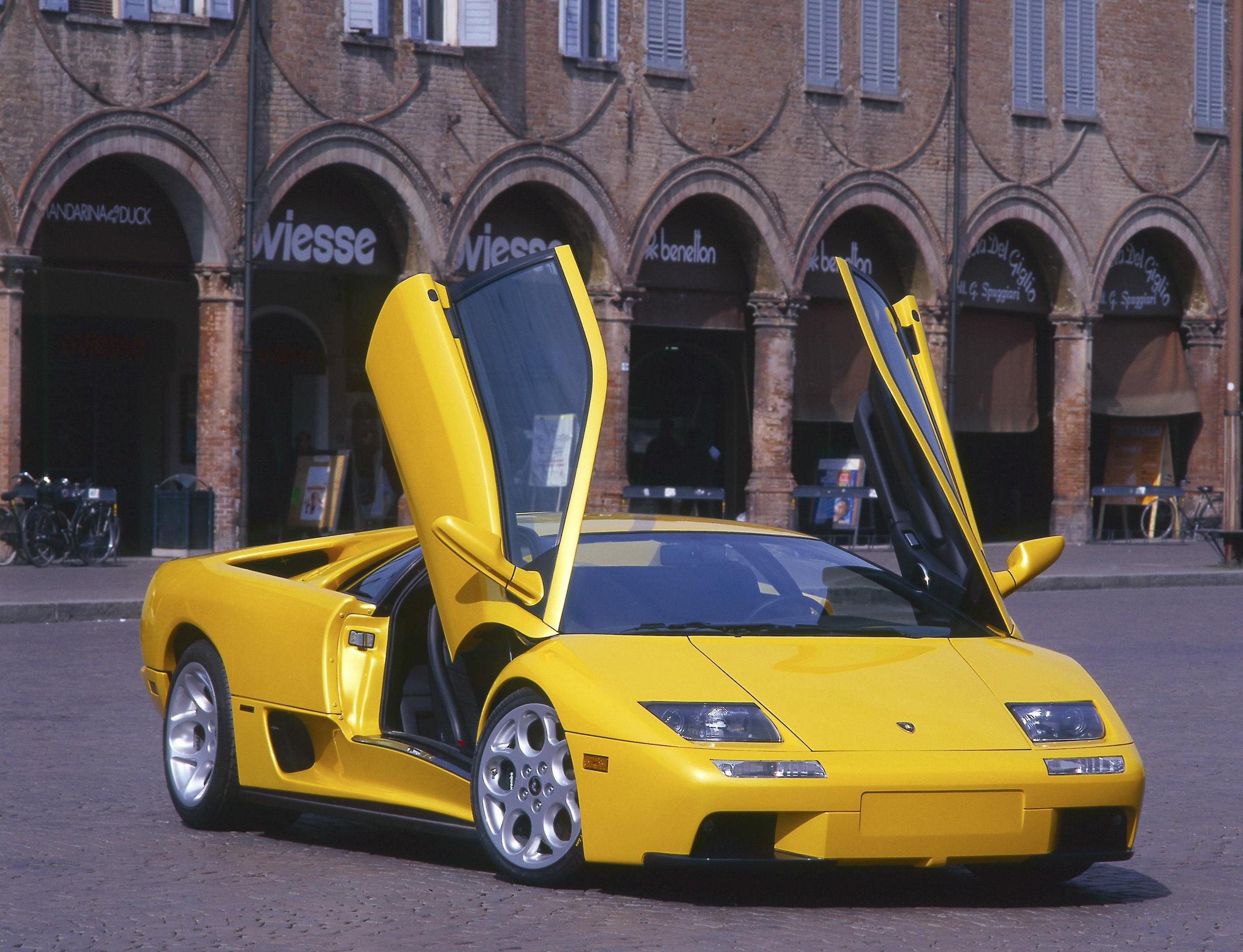 Yellow Lamborghini Diablo with scissor doors open on a cobblestone plaza in front of a historic building