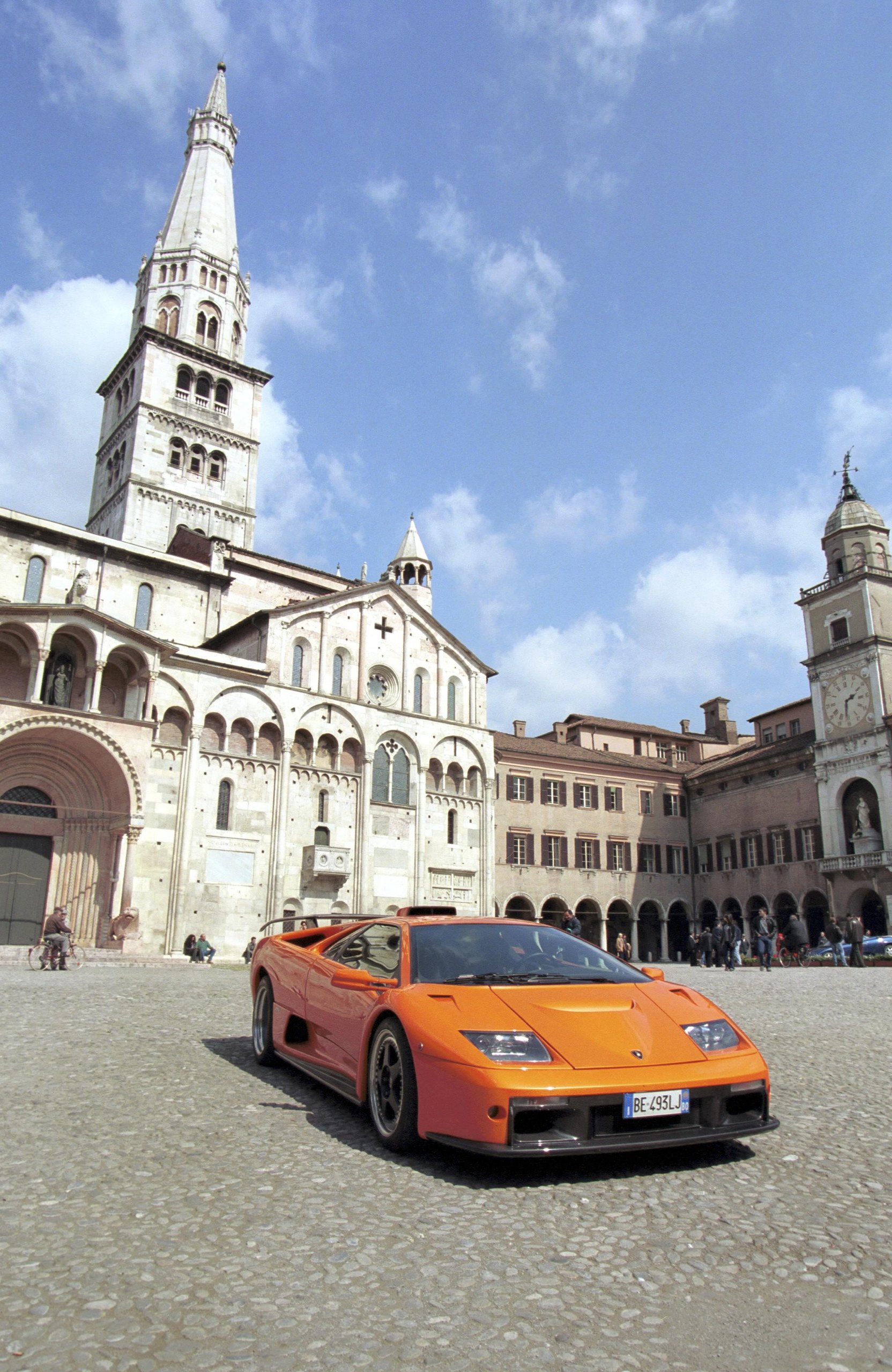 Orange Lamborghini Diablo parked in a historic European city square with a grand cathedral in the background