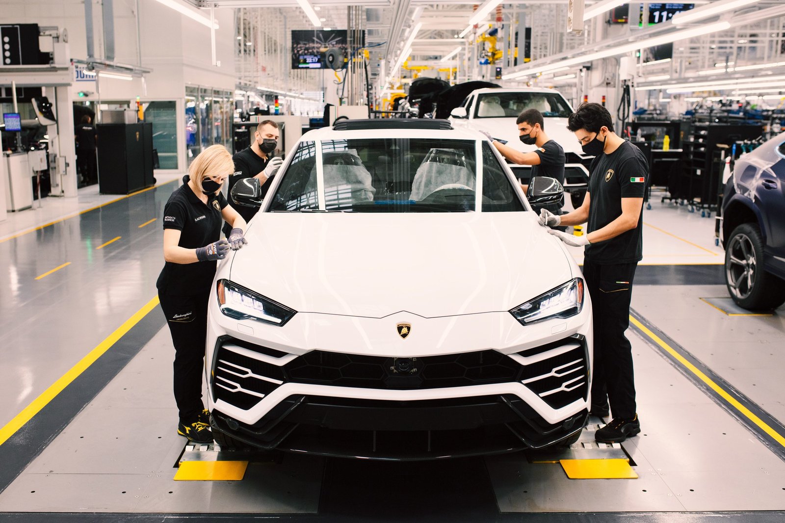 Four Lamborghini employees working on the front of a white Urus on the assembly line at Sant'Agata Bolognese