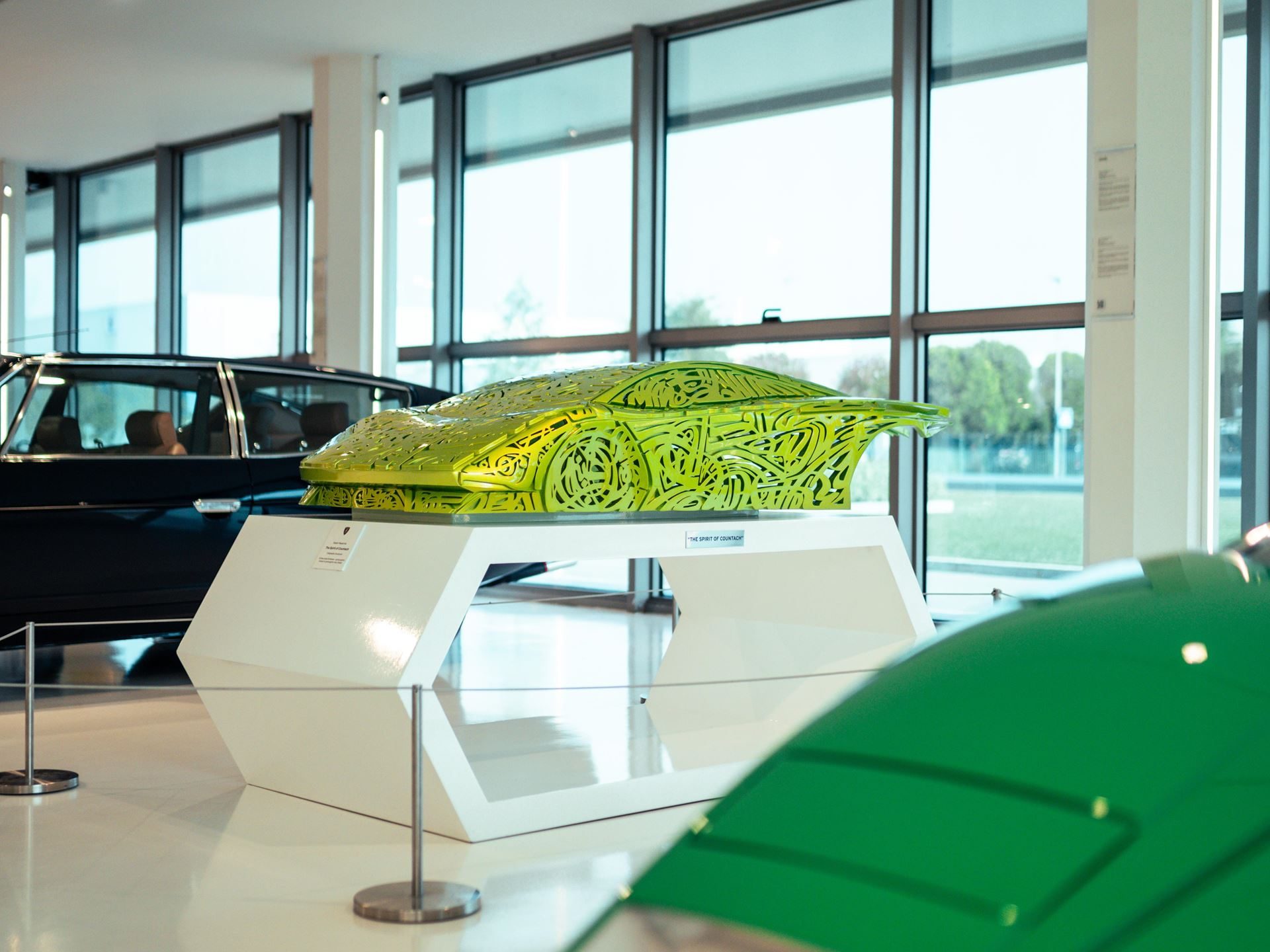 A lime green geometric sculpture resembling a lamborghini countach lp400 displayed on a white pedestal in the bright museum exhibition space