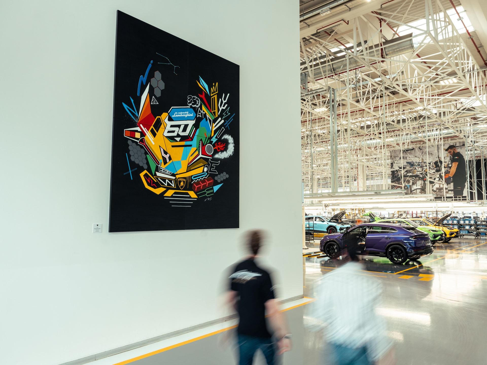 A vibrant abstract painting featuring a lamborghini urus and the number 60 displayed on a factory wall, with production vehicles visible in the background