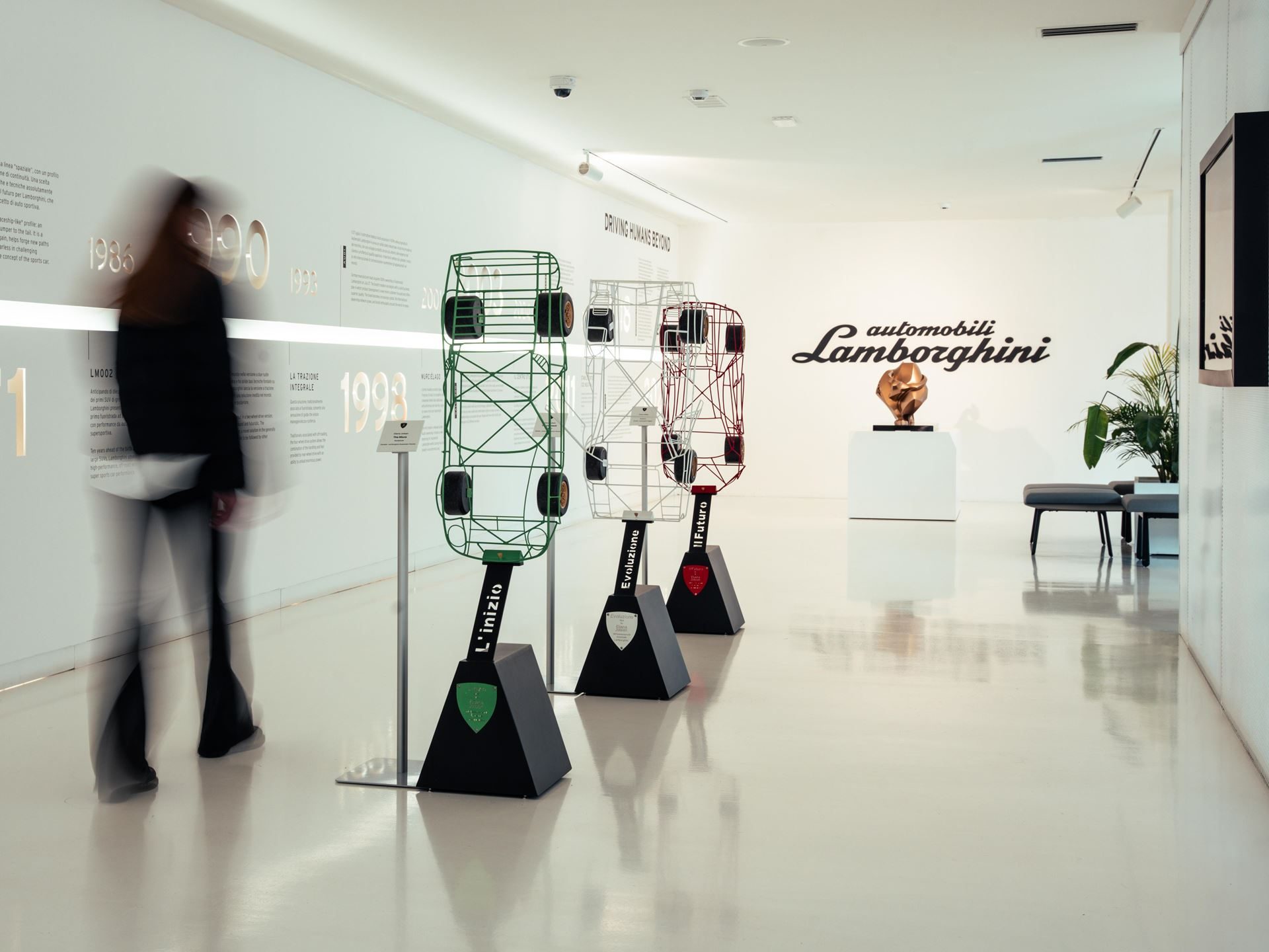 Three colorful wireframe car sculptures labeled l'inizio, evoluzione, and il futuro displayed in the dreamaway exhibition hall with a lamborghini timeline on the wall