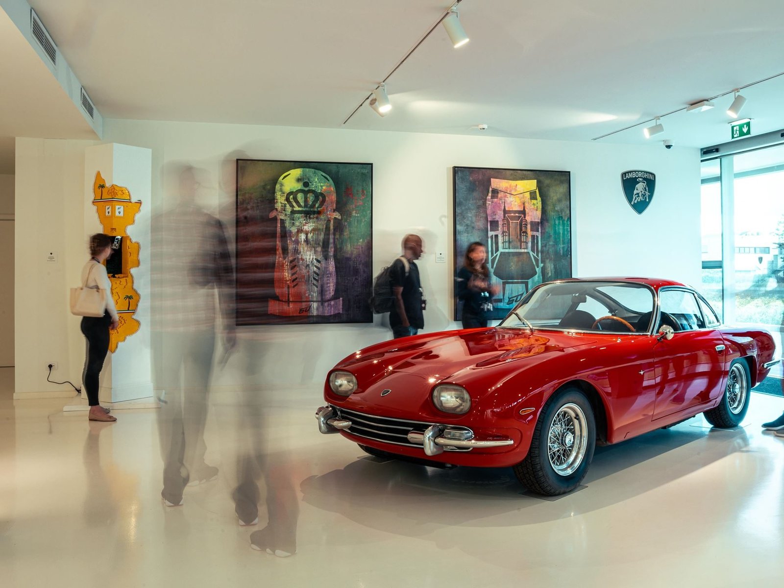 A classic red Lamborghini 350 GT displayed alongside contemporary artworks in the brightly lit Dreamaway exhibition hall at Sant'Agata Bolognese