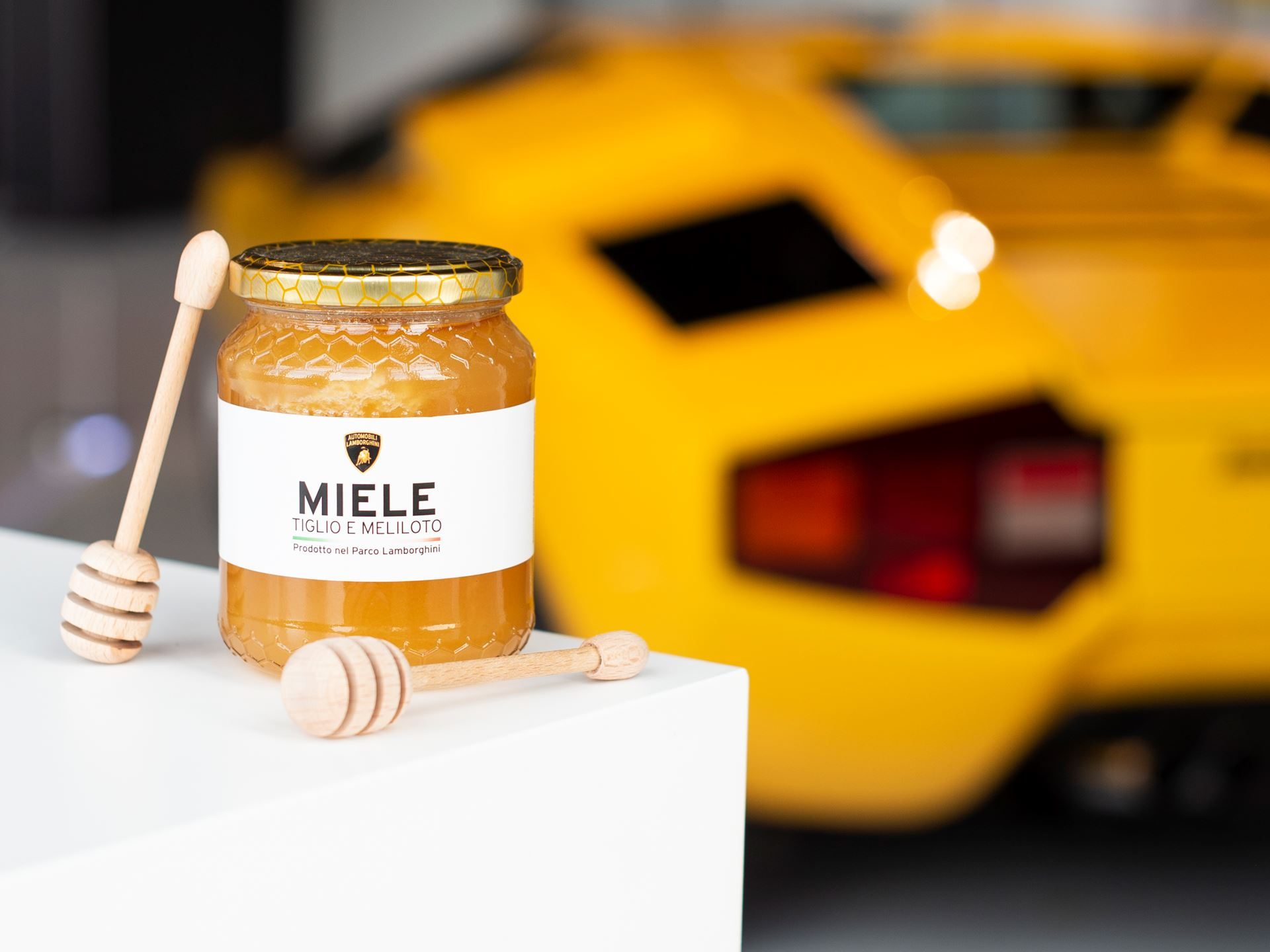 Bees, Biogas, And The Raging Bull: How Lamborghini'S Factory Sustainability Protects Its Performance Future 3 Lamborghini-branded honey jar with wooden dippers displayed in front of a blurred yellow lamborghini countach