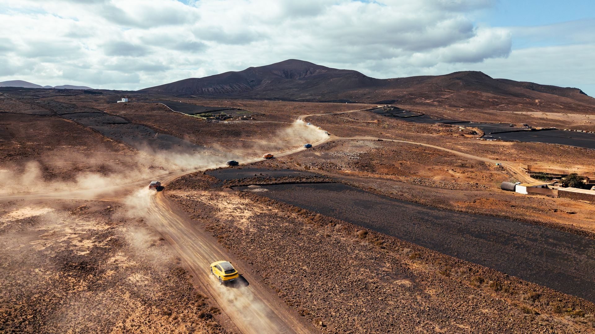 Multiple lamborghini urus suvs driving through a vast volcanic landscape on dusty dirt roads