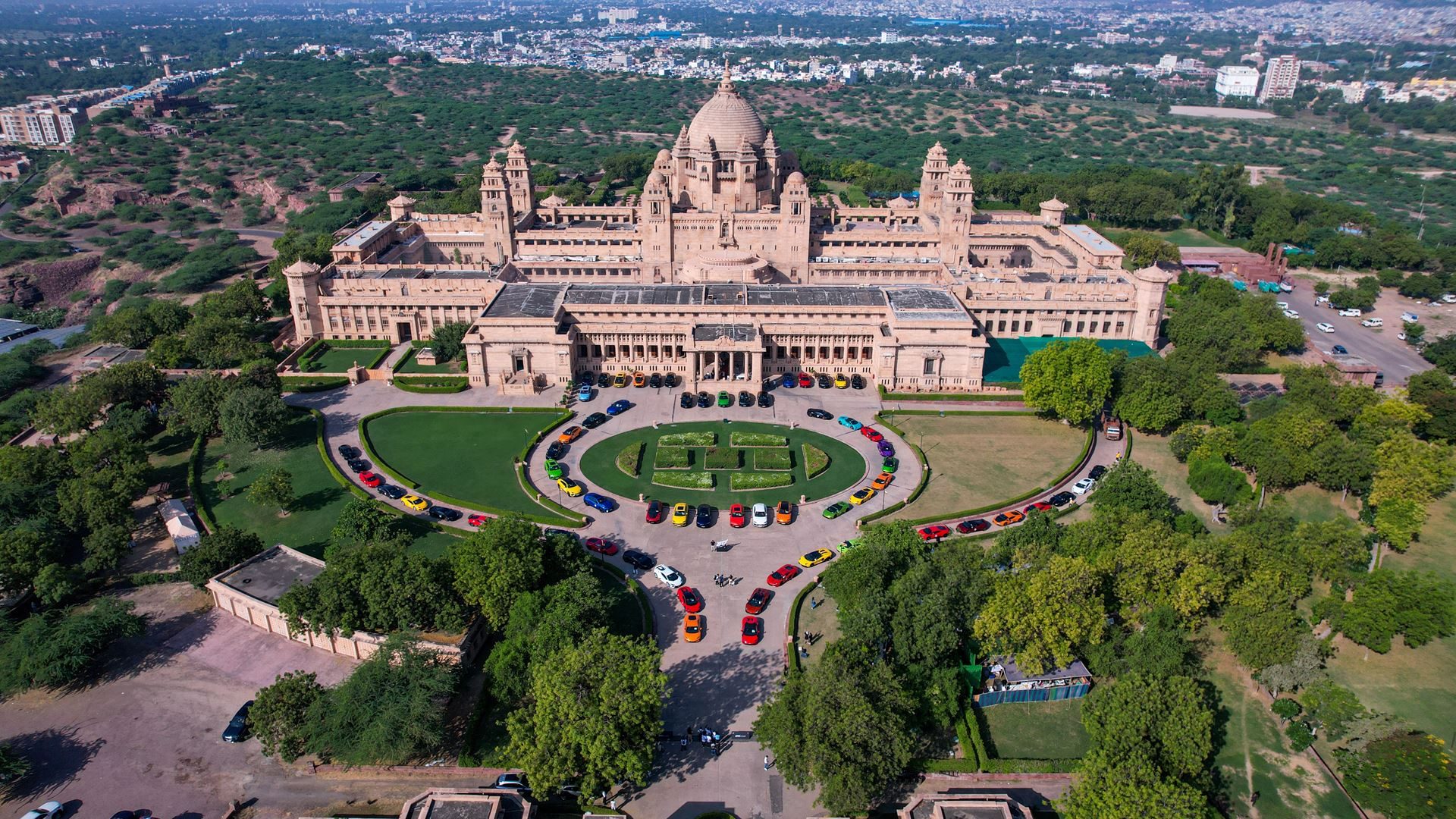 Aerial view of colorful lamborghini vehicles parked in formation on the lawn of an ornate european palace during an esperienza event