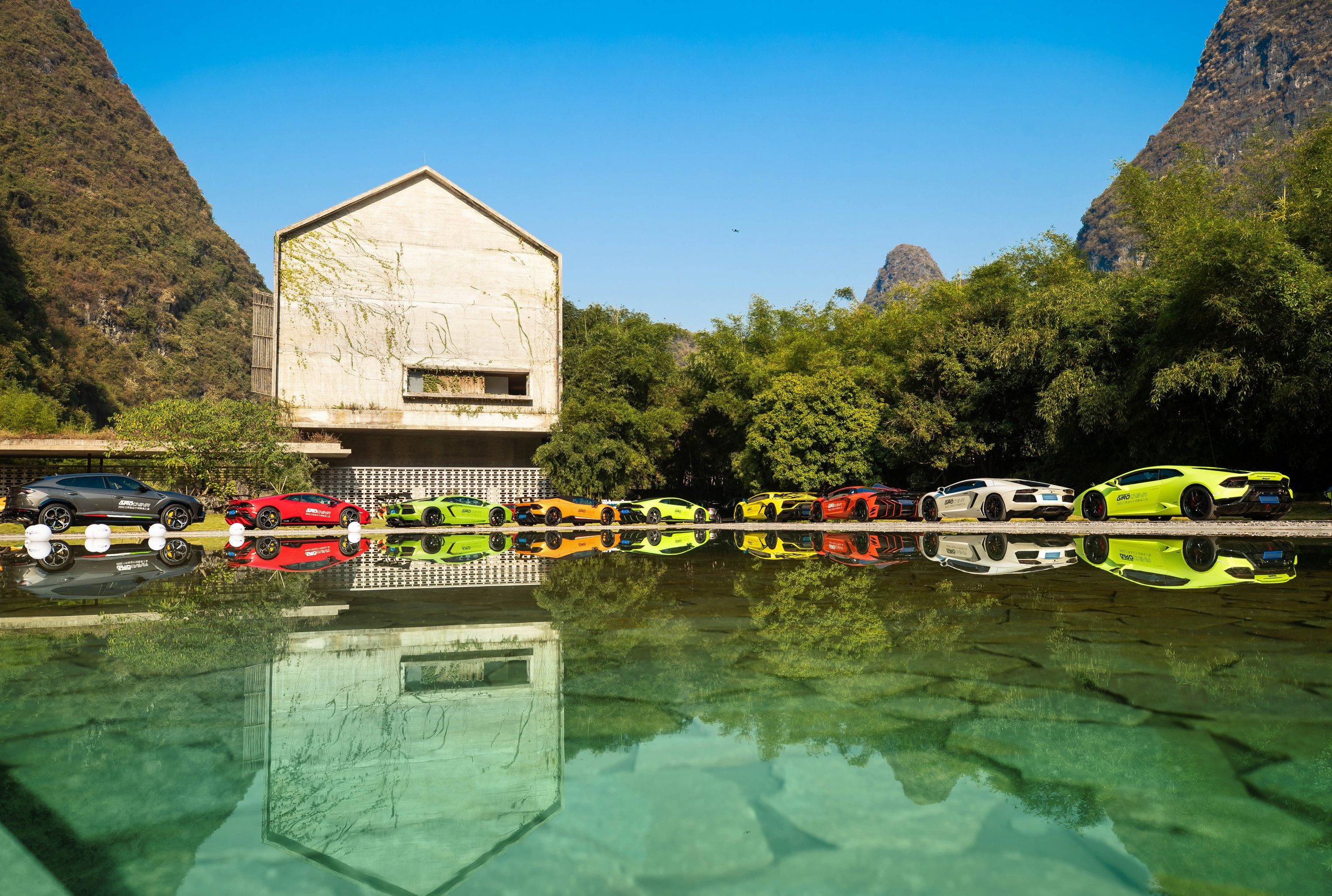 1,100 Kilometers Through Karst Country: How Lamborghini Turned Southern China Into A Rolling Showroom 11 Line of colorful lamborghini vehicles including huracáns and urus reflected in water with karst mountains in background