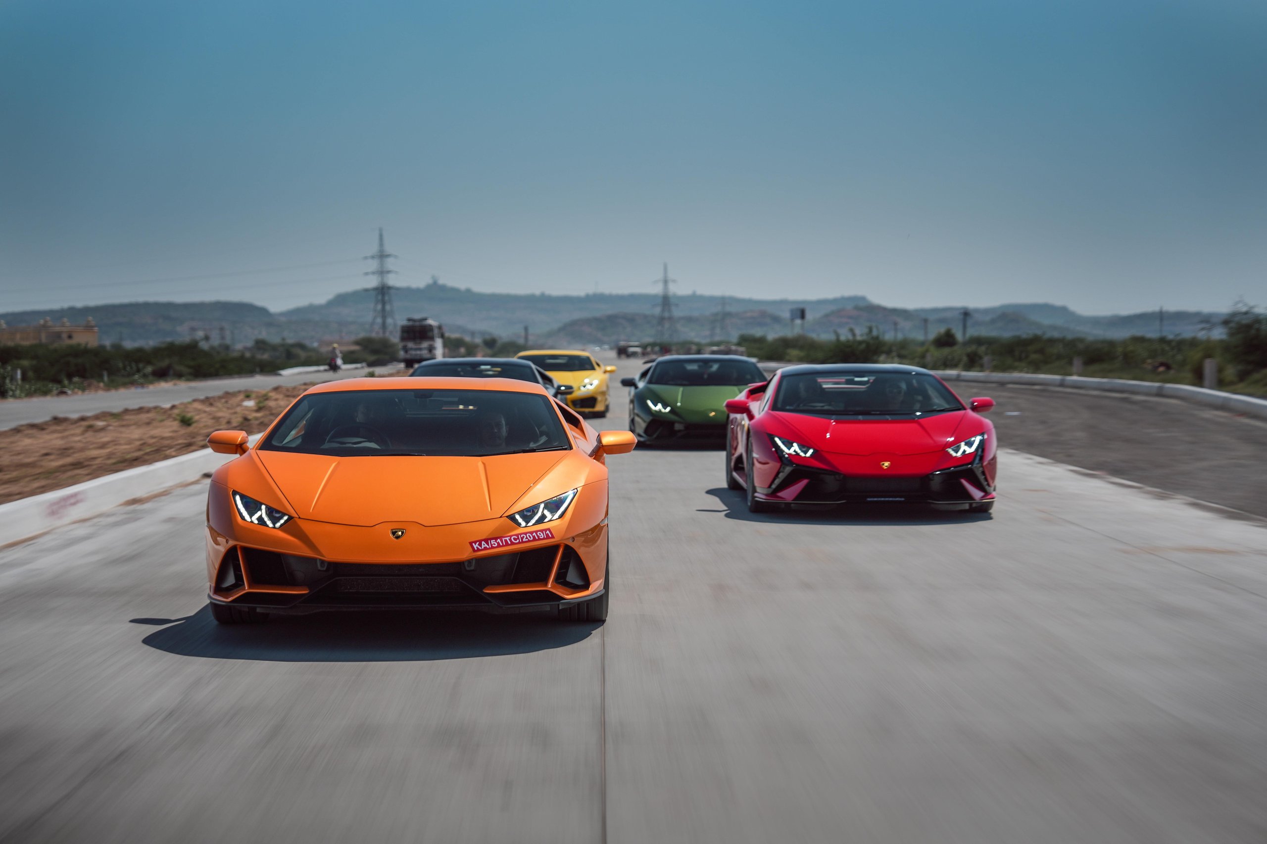 Lamborghini Esperienza Giro India 2023: A Royal 60Th Anniversary Celebration Across Rajasthan 5 Orange lamborghini huracán leading a colorful convoy of lamborghinis on a paved road through rajasthan's arid rural landscape