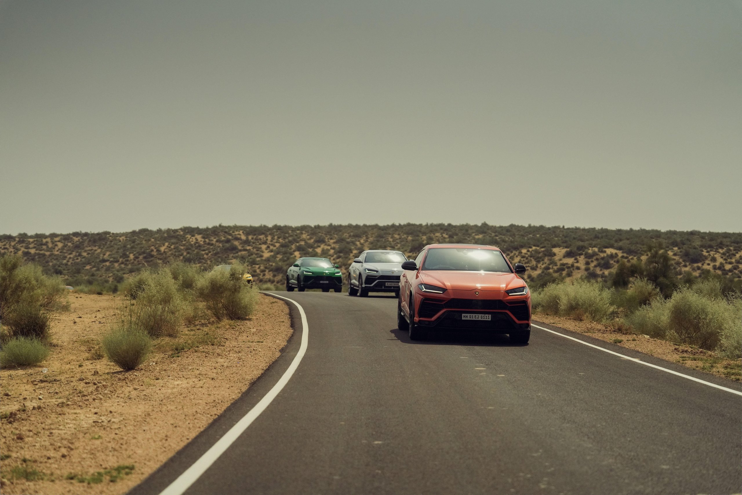Lamborghini Esperienza Giro India 2023: A Royal 60Th Anniversary Celebration Across Rajasthan 11 Orange lamborghini urus leading a convoy of urus models on a winding road through dry rajasthani landscape