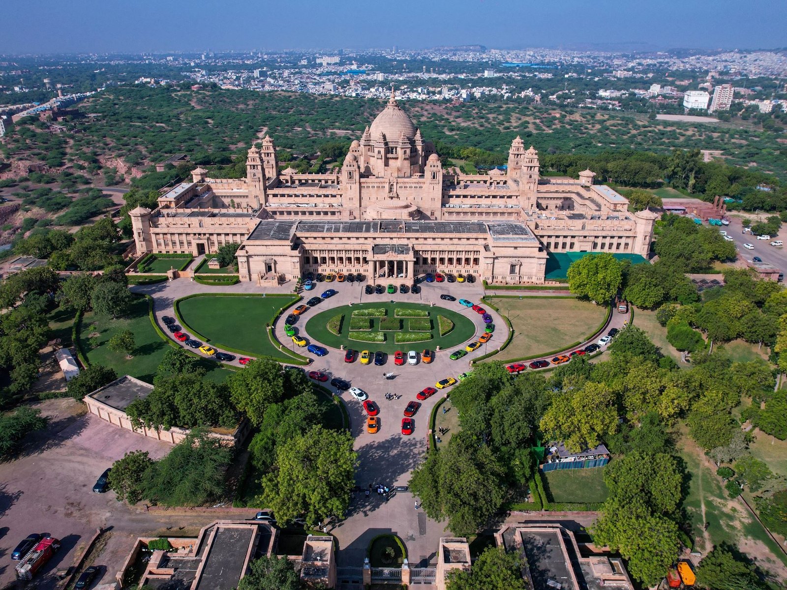 Aerial view of more than 60 colorful Lamborghini cars parked in a circular formation on the lawn of a grand Rajasthani palace