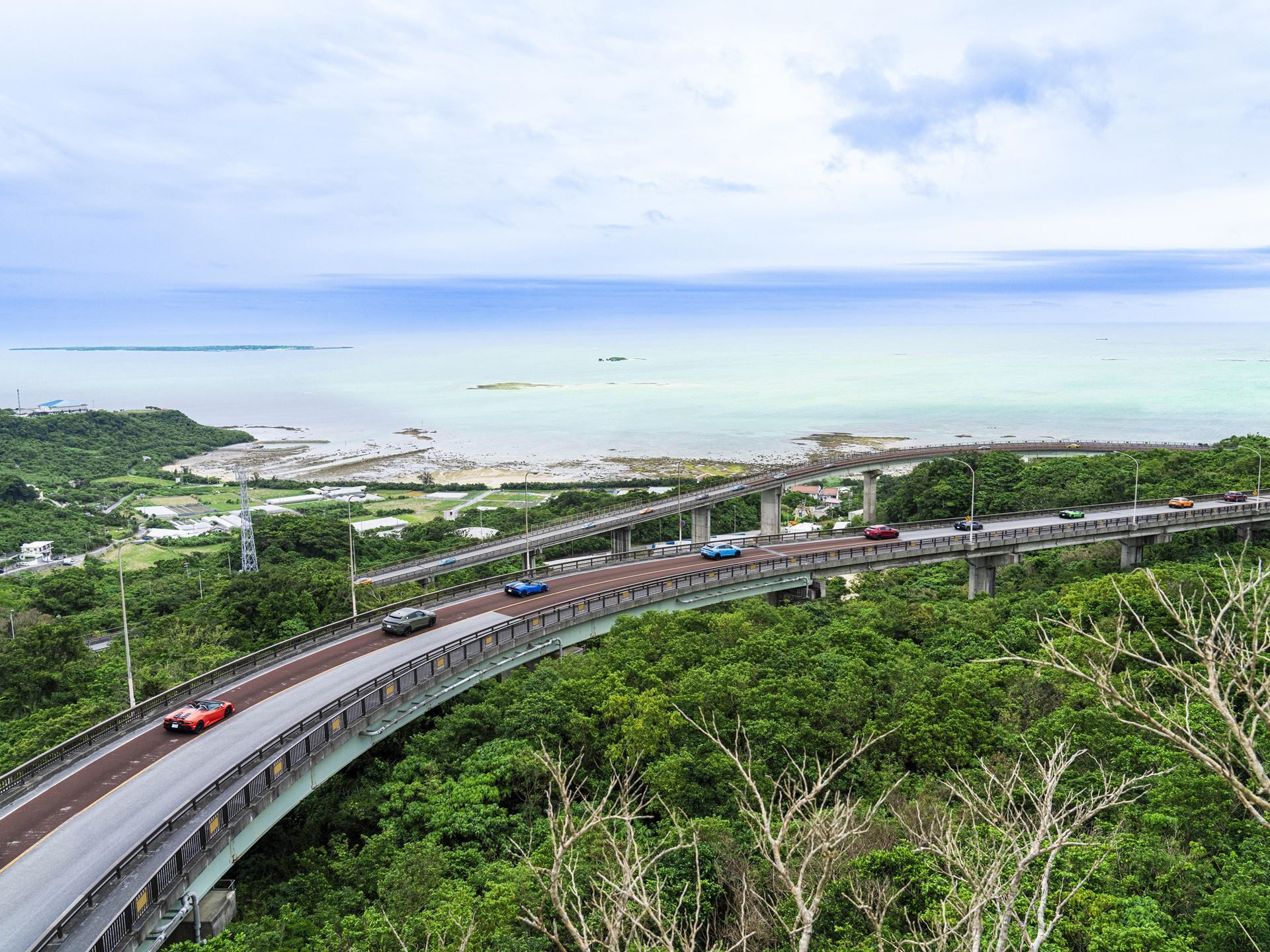 Lamborghini Turned Okinawa Into A Three-Day Supercar Convoy For Giro Japan 2024, With A Revuelto Debut As The Centerpiece 3 Aerial view of a winding coastal highway with a convoy of lamborghini vehicles driving along it overlooking the ocean