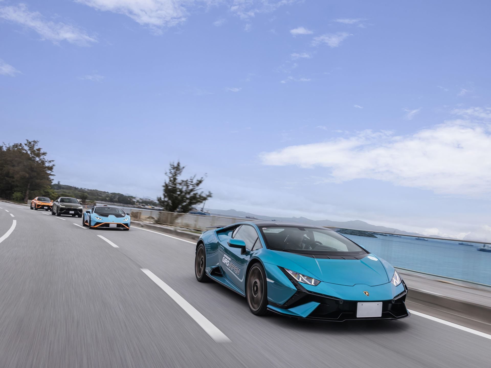 Lamborghini Turned Okinawa Into A Three-Day Supercar Convoy For Giro Japan 2024, With A Revuelto Debut As The Centerpiece 9 A teal lamborghini huracán leading a convoy of other lamborghinis down a scenic coastal road with the ocean visible