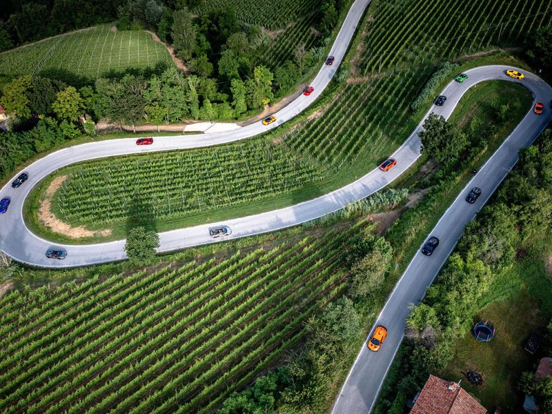 Aerial view of multiple Lamborghini supercars driving on a winding road through green vineyards in Piedmont, Italy