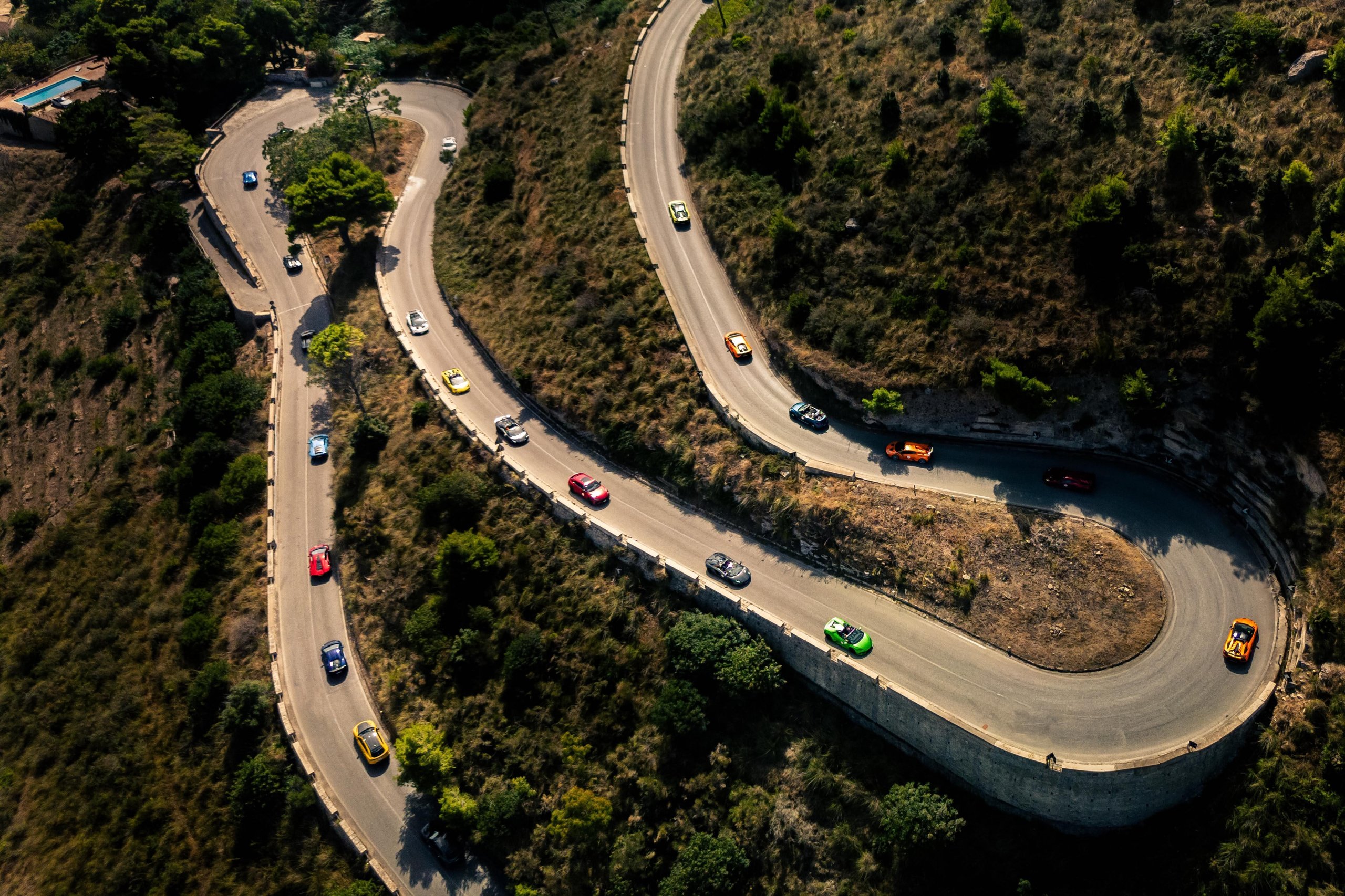 Esperienza Giro Sicilia: How Lamborghini Turned 750 Km Of Ancient Roads Into Its Most Personal Anniversary Statement 7 Aerial view of colorful lamborghini huracán models navigating tight hairpin turns on a winding mountain road surrounded by lush green trees