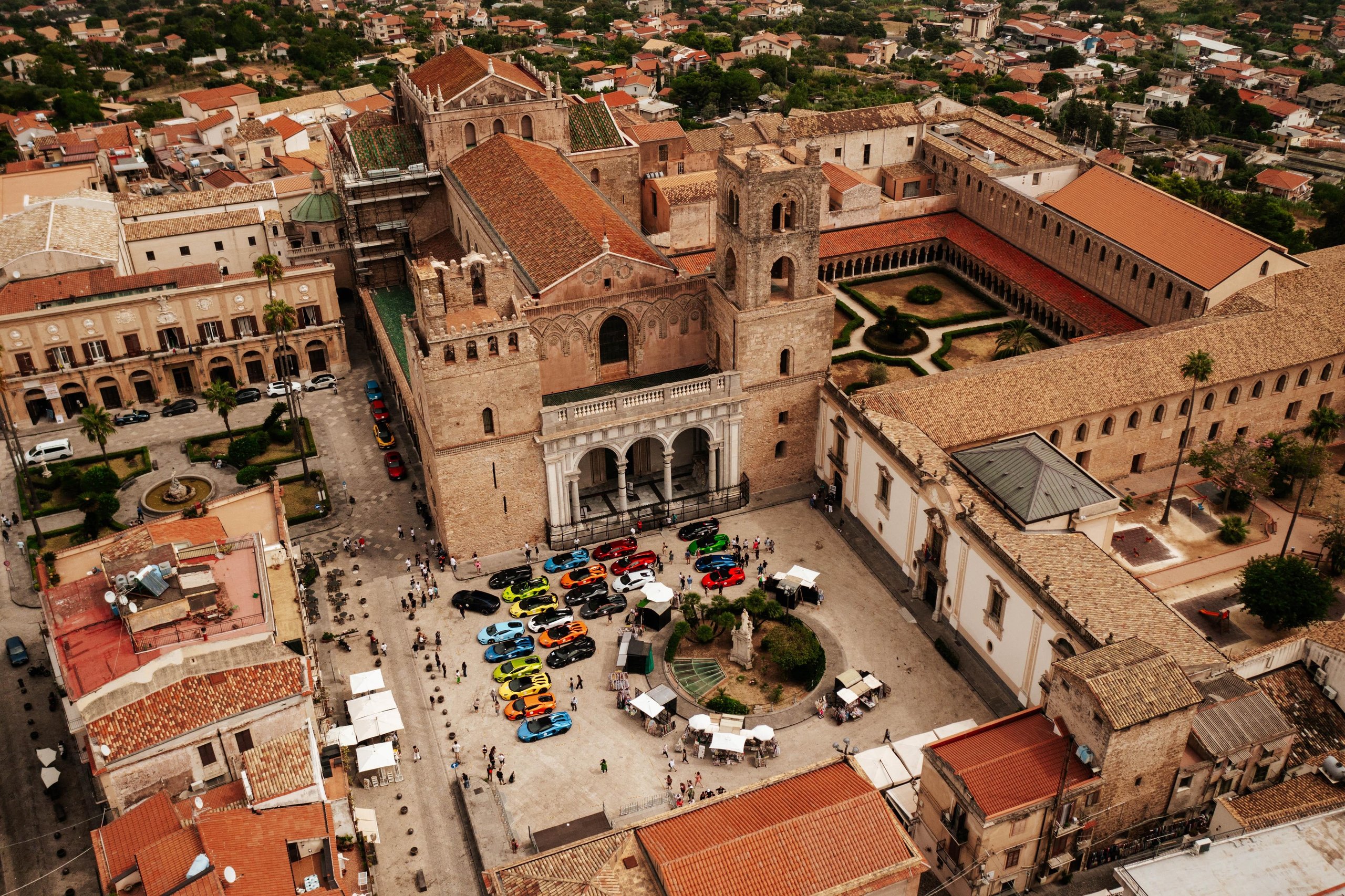 Esperienza Giro Sicilia: How Lamborghini Turned 750 Km Of Ancient Roads Into Its Most Personal Anniversary Statement 3 Aerial view of colorful lamborghini huracán and urus models parked in a historic sicilian town square in front of a grand cathedral, surrounded by spectators
